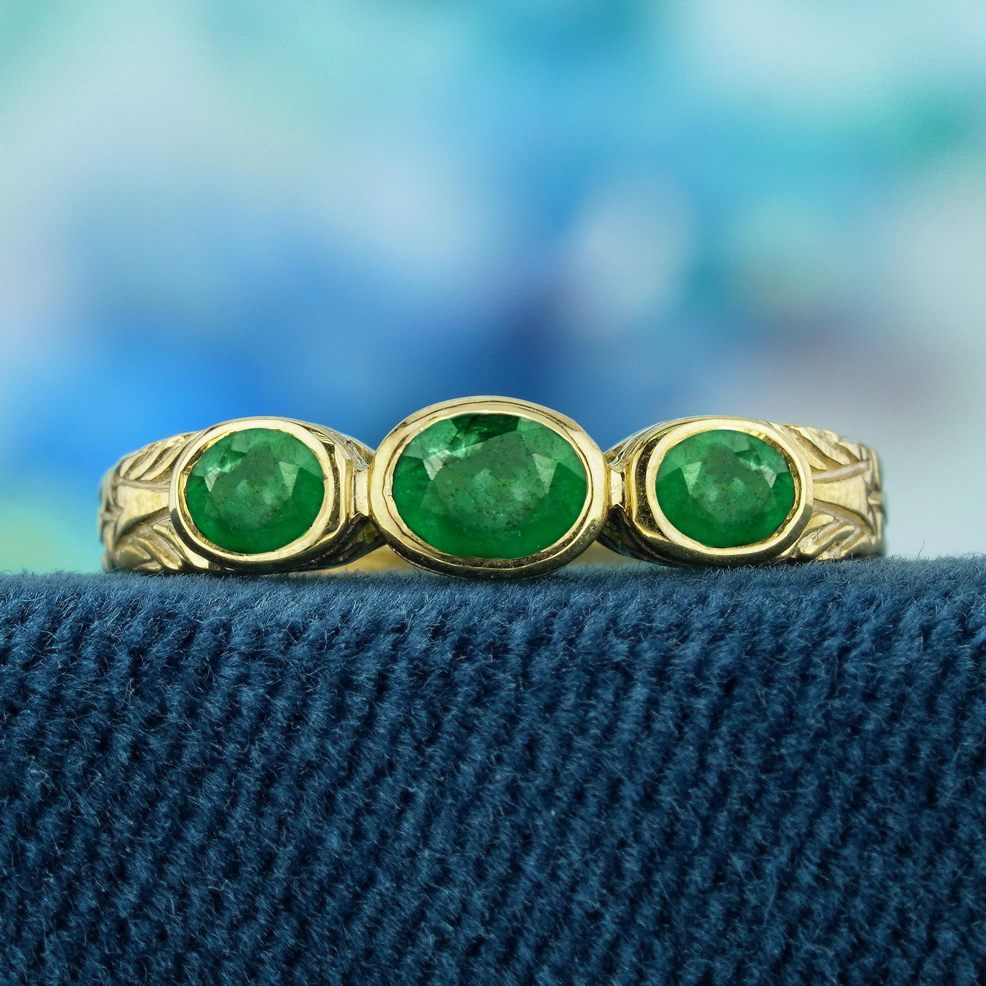 The ring features a vintage style, characterized by intricate detailing and a timeless aesthetic. The yellow gold setting offers a warm and rich backdrop for the gemstones. At the heart of the ring are three natural oval-cut vibrant green emeralds