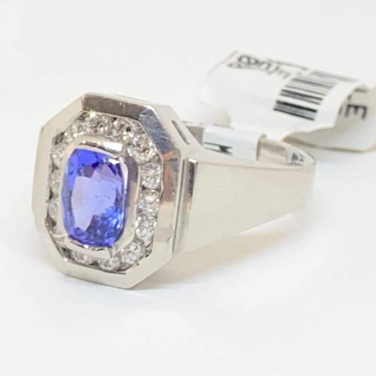 Natural tanzanite half-bezel set with a round diamond halo surrounding the center. Designed in platinum with a wide polished shank. The diamonds are channel set in an octagon shape. 

Center: Natural Tanzanite
Shape: Oval Brilliant
Weight: 1.01
