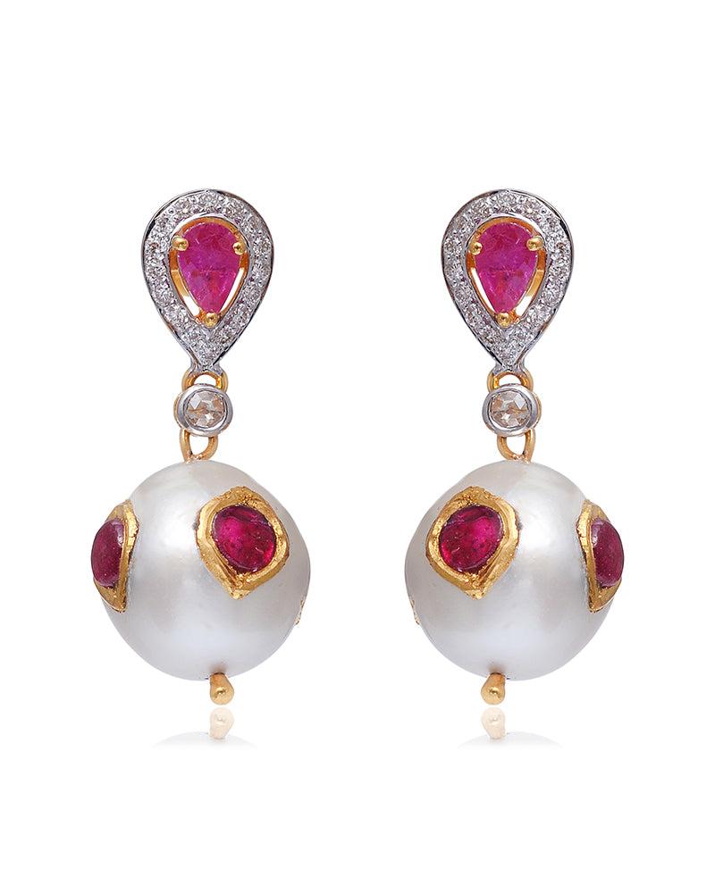 Elegance but make it quirky. These unique dangle earrings have a charm of their own because of the innovative use of rubies encrusted in pearls. Set in 18K solid yellow gold, the piece also features 0.28-carat natural diamond. Truly a piece that can