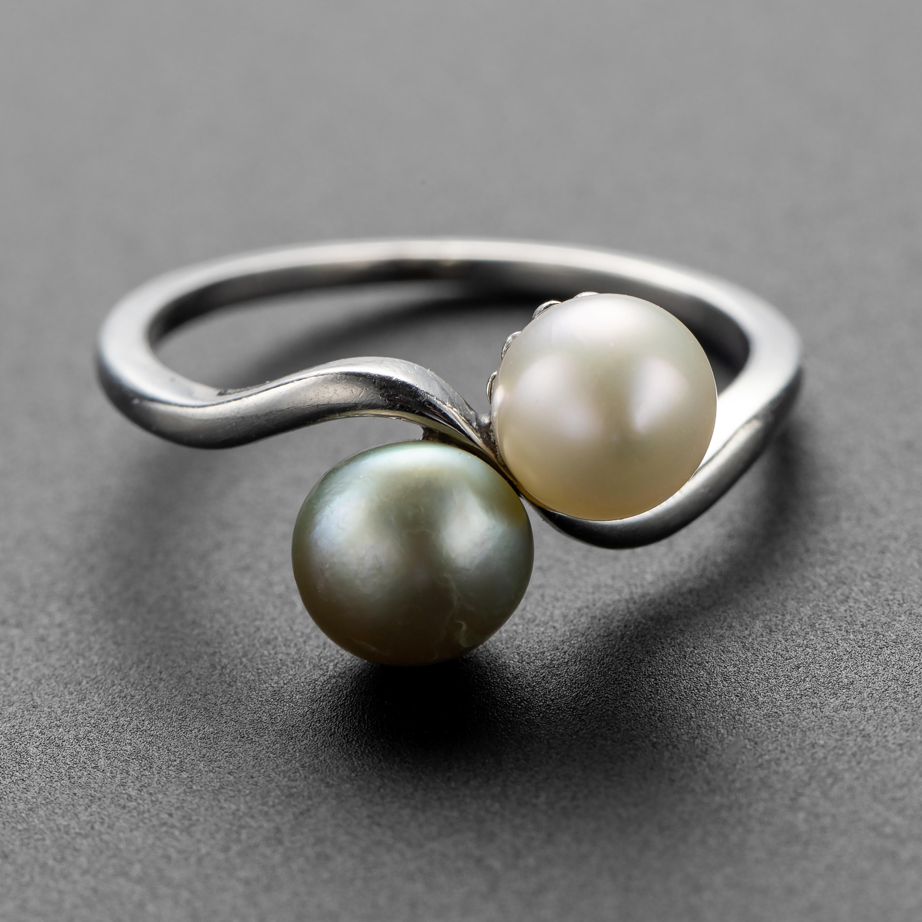 This rare and wonderful Art Deco ring features a pair of luminous natural, uncultured saltwater pearls. White and light gray in tone, the pearls reside on their handmade platinum setting, which is a gleaming cool pewter tone. The platinum band has