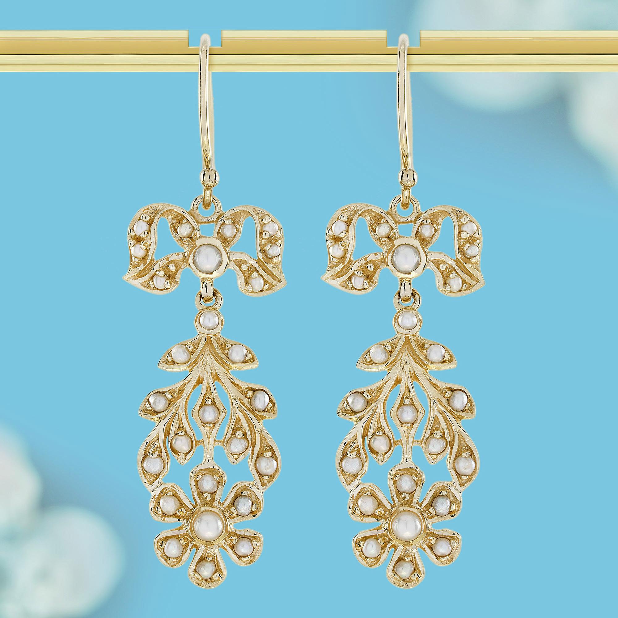 These dangling earrings showcase a delightful floral motif crafted from yellow gold frames. At the top, charming round white pearls in a gold ribbon shape enhances the overall aesthetic with its delicate detail. Towards the bottom, round white