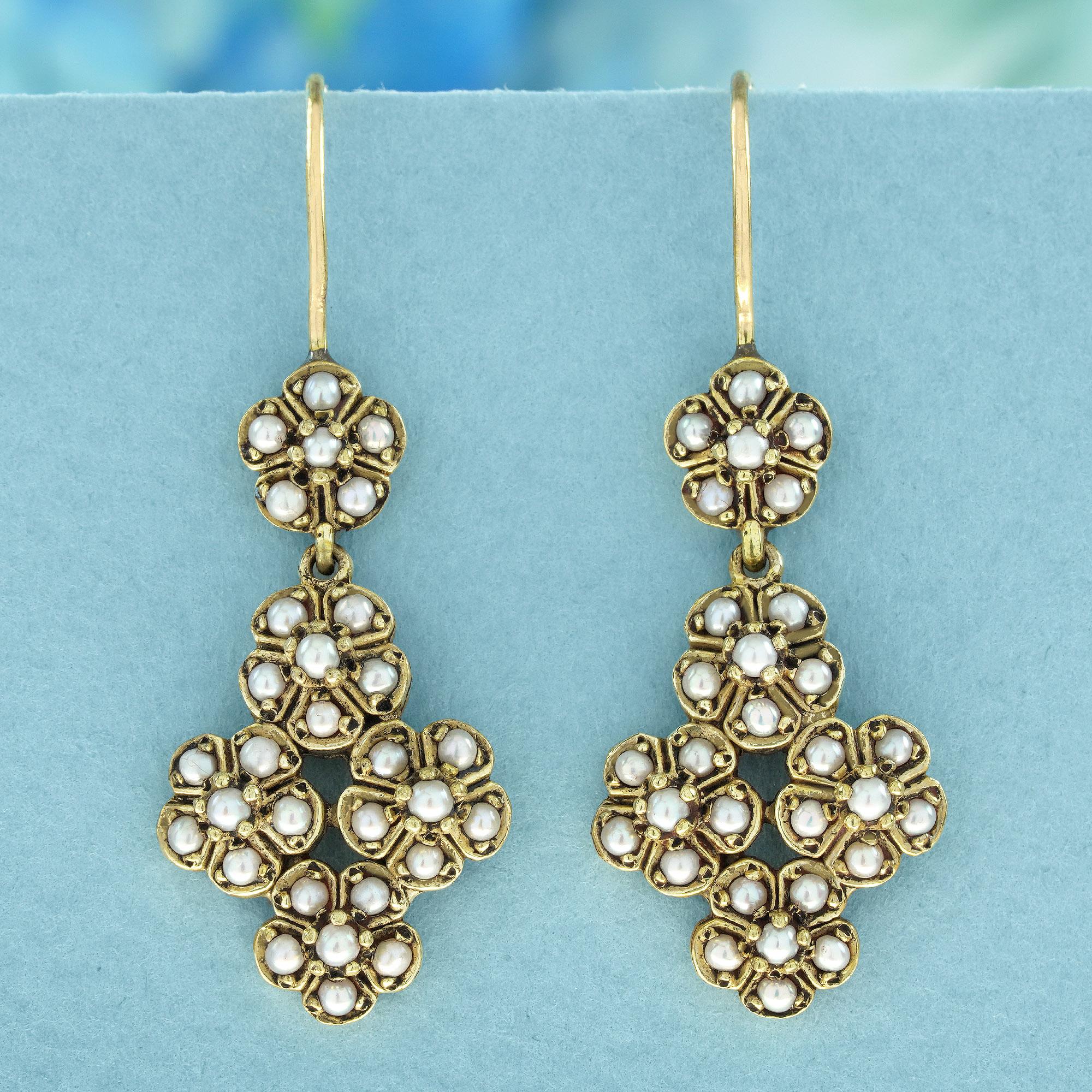 These dangling earrings feature a charming floral design crafted from yellow gold frames, delicately forming petals and leaves reminiscent of blooming clusters of flowers. Each earring is adorned with round white pearls in prong settings,
