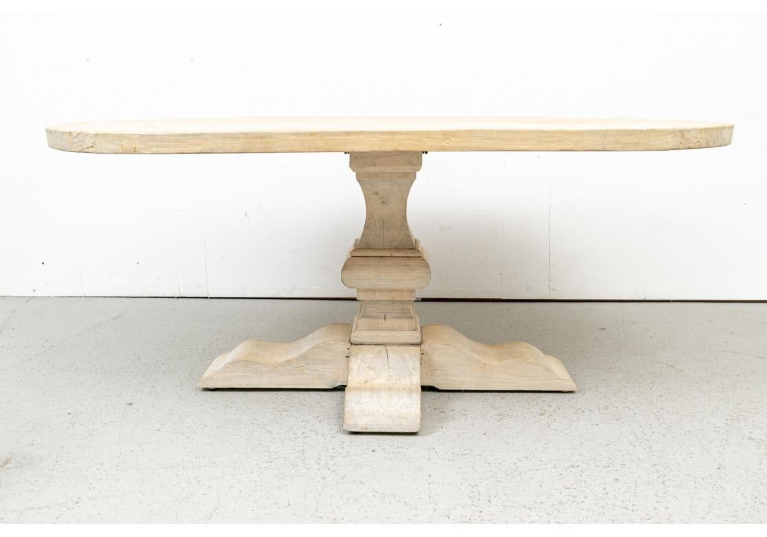 A large oval table unfinished in natural pine with an angular baluster support mounted on four wide shaped flat feet. 
Measures: L. 72