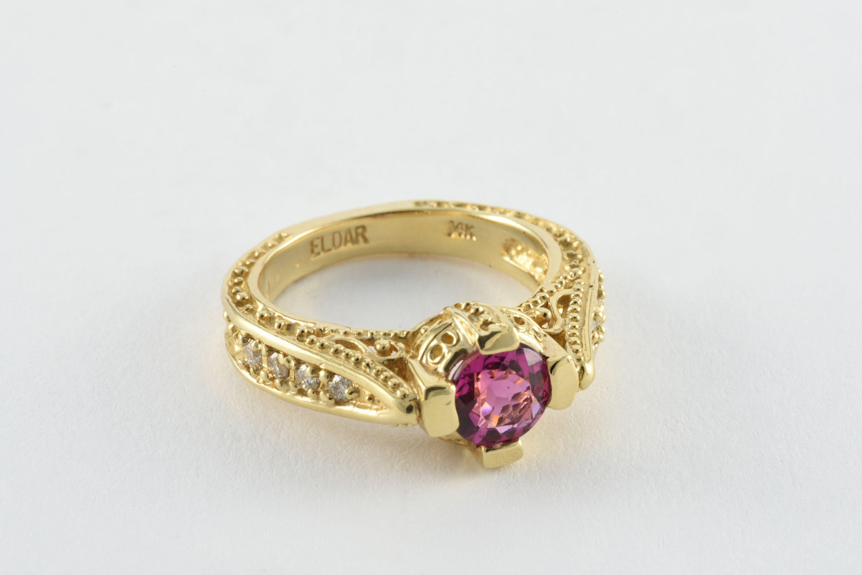 A natural pink round-shaped tourmaline measuring approximately 0.97 carats is the centerpiece of this ornate modern band fashioned from 14kt yellow gold with decorative swirling piercing, delicate milgraining and elaborate etching. The sides are