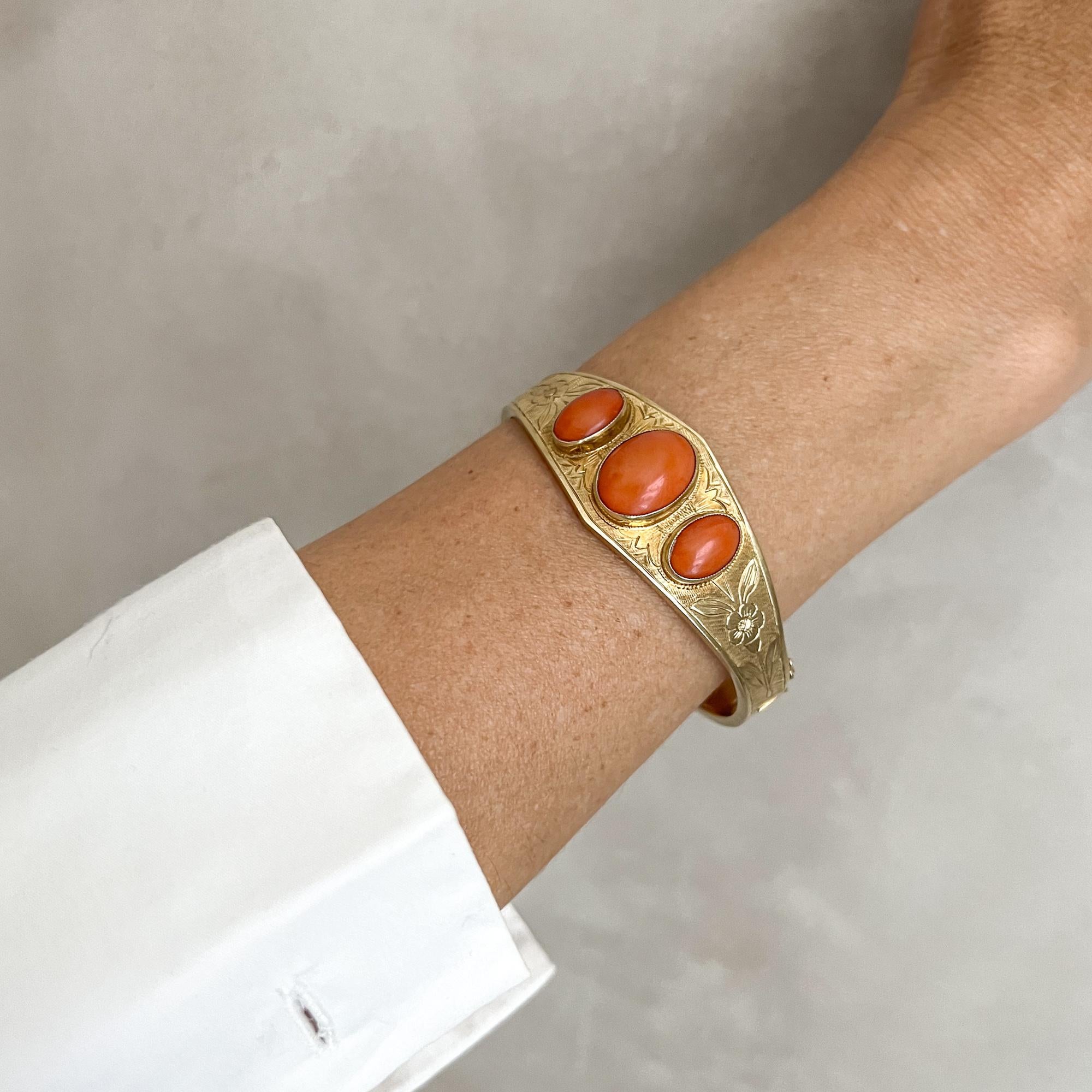 Ce bracelet en or jaune 14 carats est serti de trois pierres naturelles en corail rouge. Ce bracelet artisanal de style Art déco est serti de trois pierres de corail naturel de forme ovale taillées en cabochon. Les pierres précieuses sont toutes