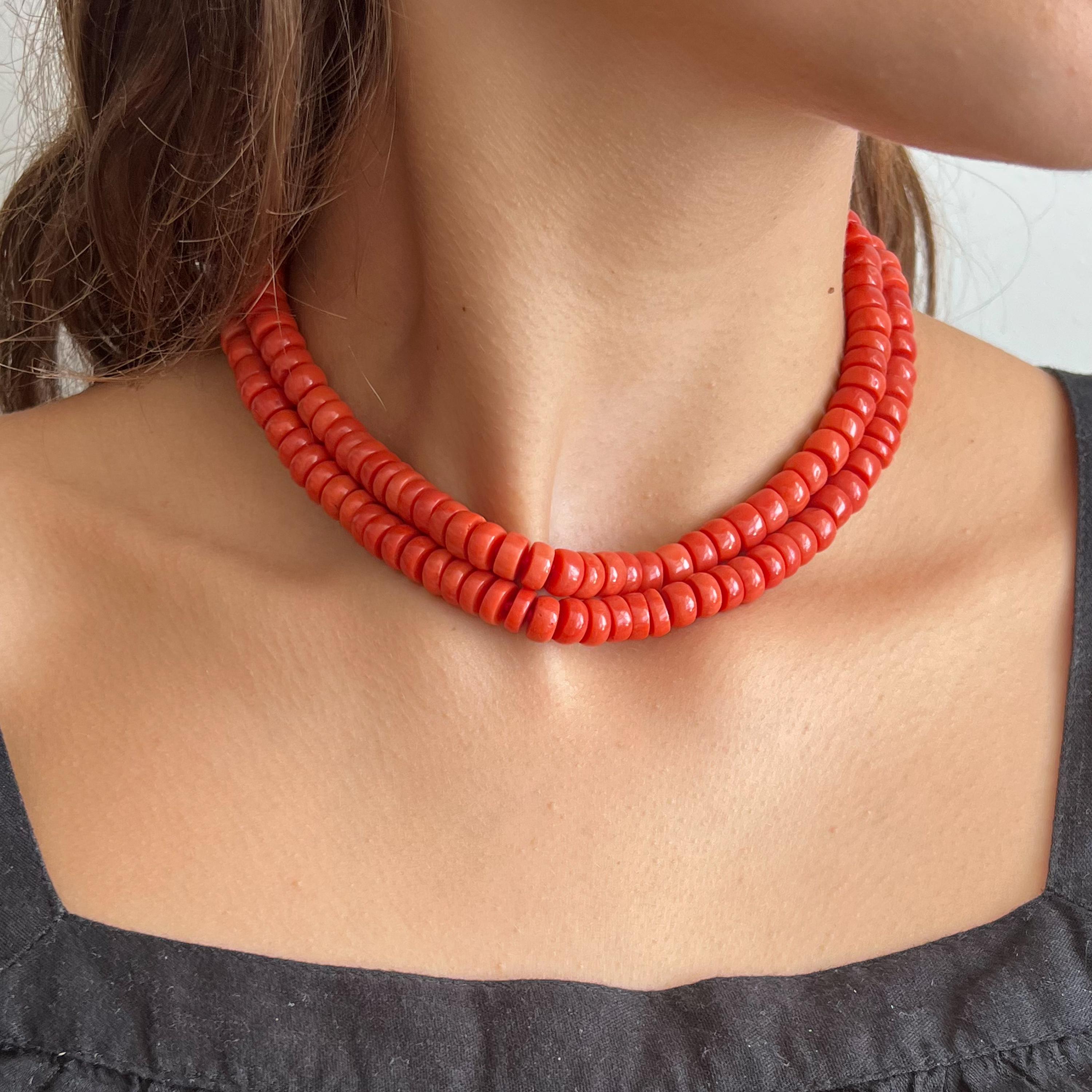 A natural coral and 14 karat gold two-strand beaded necklace. The coral beads of this necklace are barrel-shaped and set with a beautiful oval-shaped clasp created in 14 karat gold. The clasp is set with a smooth oval-shaped coral cabochon stone,