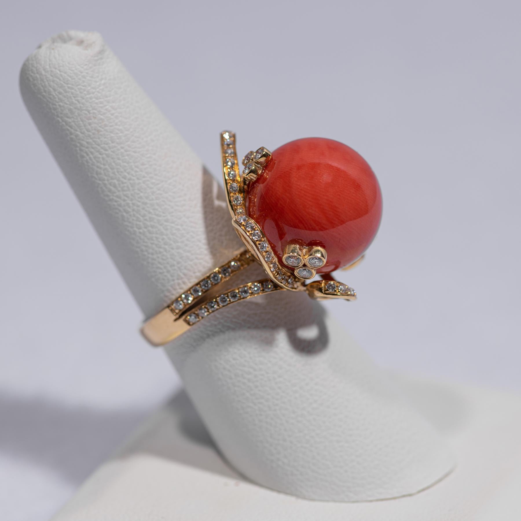 A beautiful ring of natural red orange coral set in 18k yellow gold and mounted with diamonds. Ring size 7

The ring centered around a large round coral bead of exceptional and even reddish orange color surrounded by an undulating ribbon setting in