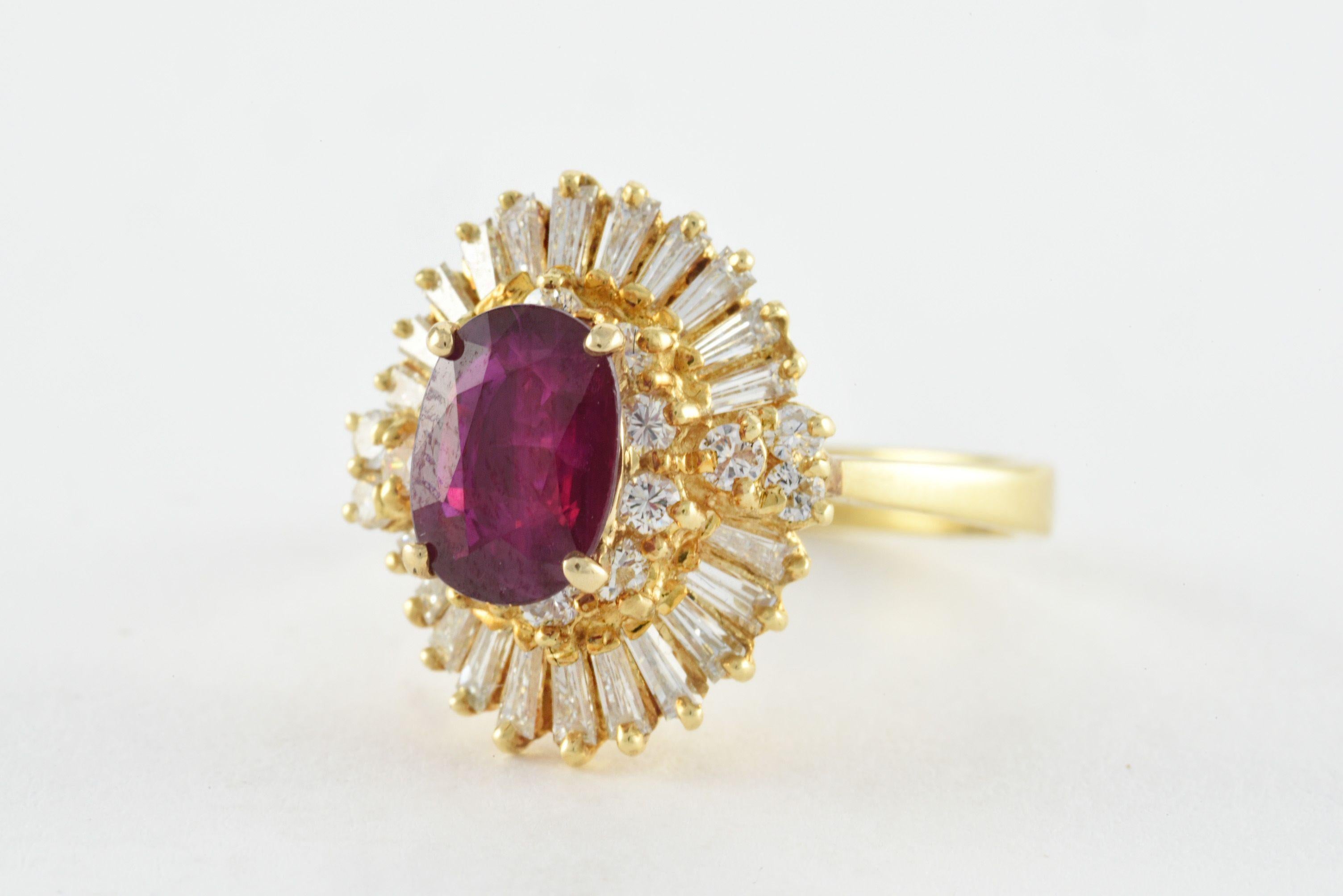A natural oval-shaped red ruby measuring approximately 1.30 carats sits at the center of this striking ballerina ring surrounded by a mix of baguette and round shaped diamonds totaling approximately 1.09 carats atop a decorative openwork under
