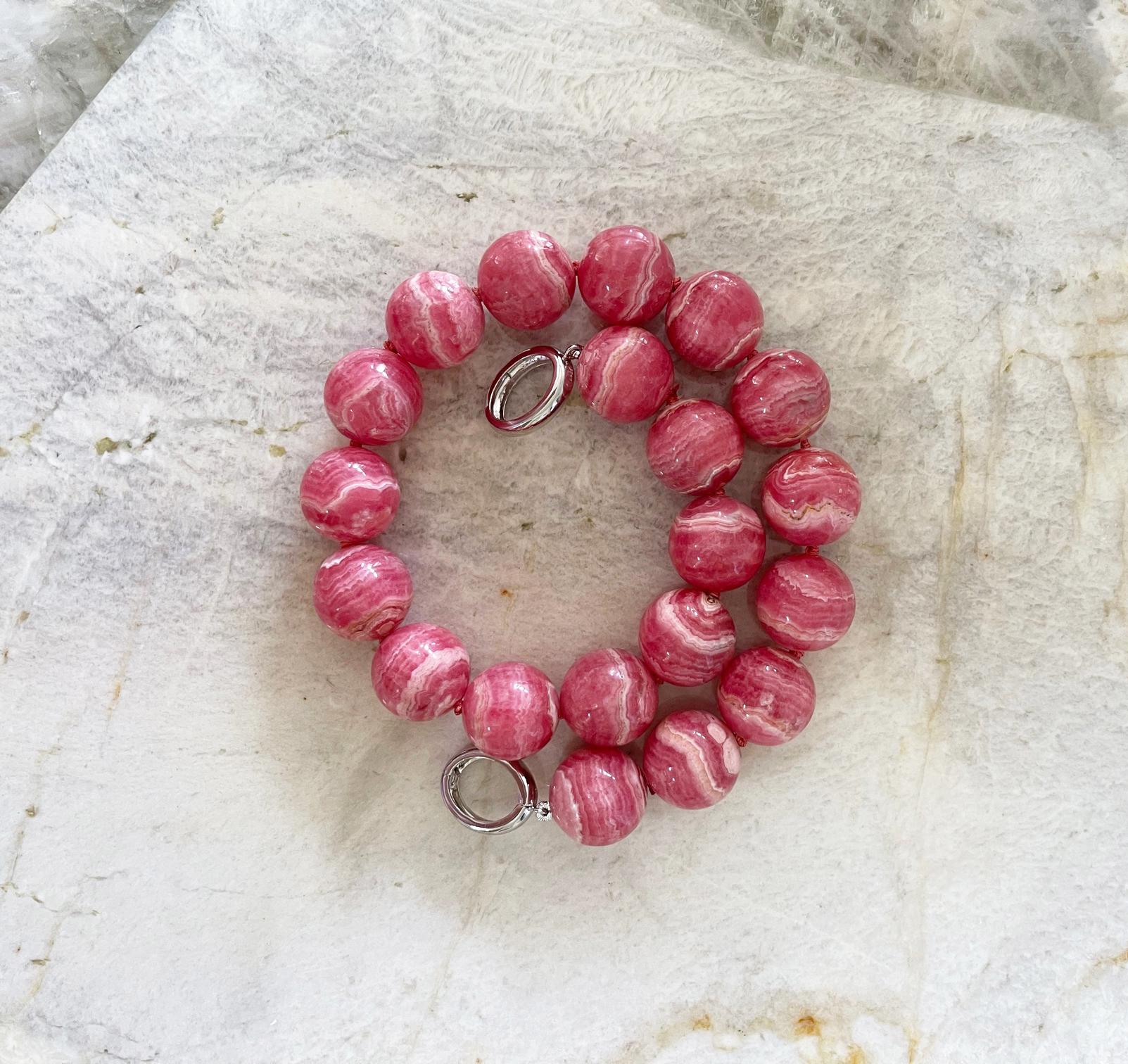 This is a truly spectacular top quality natural rhodochrosite necklace comprised of hand knotted 20mm round natural rhodochrosite beads and an elegant sterling silver interlocking clasp with rhodium plating to prevent tarnishing. We love this clasp