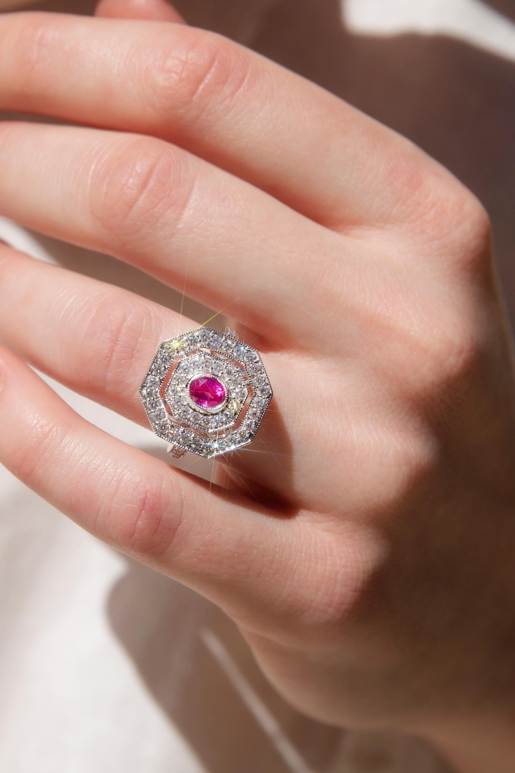 Crafted with love and devotion, this captivating 18 carat white gold milgrain cluster ring features an alluring central oval natural ruby with a double hexagonal border set with a plethora of shimmering round brilliant cut diamonds and with further