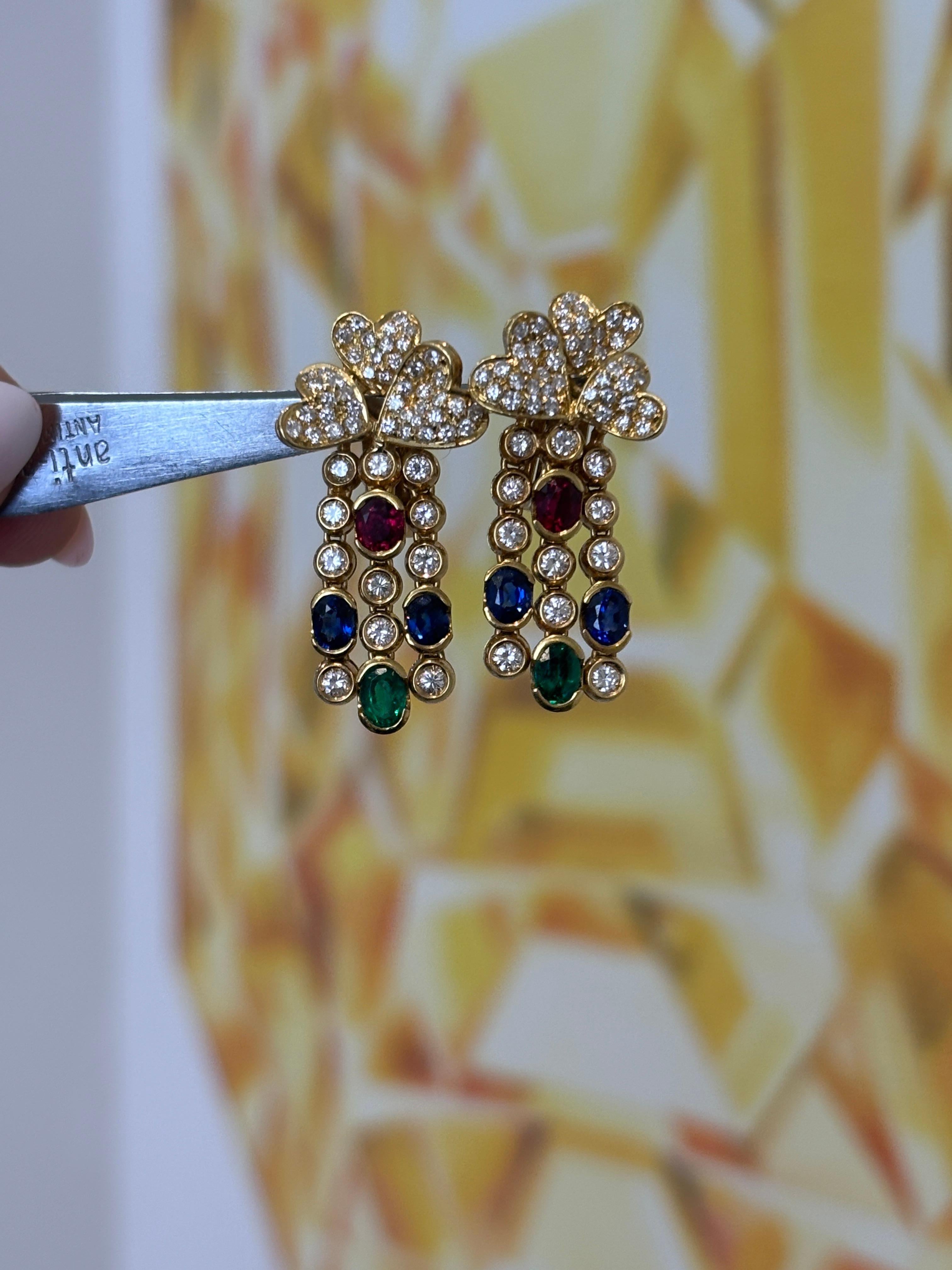 Offered is a stunning pair of vintage 18K yellow gold dangle earrings featuring vibrant rubies, sapphires, emeralds, and diamonds in a cascading heart or flower motif. The earrings are stamped 750 and have a total gem-set weight of 17.16
