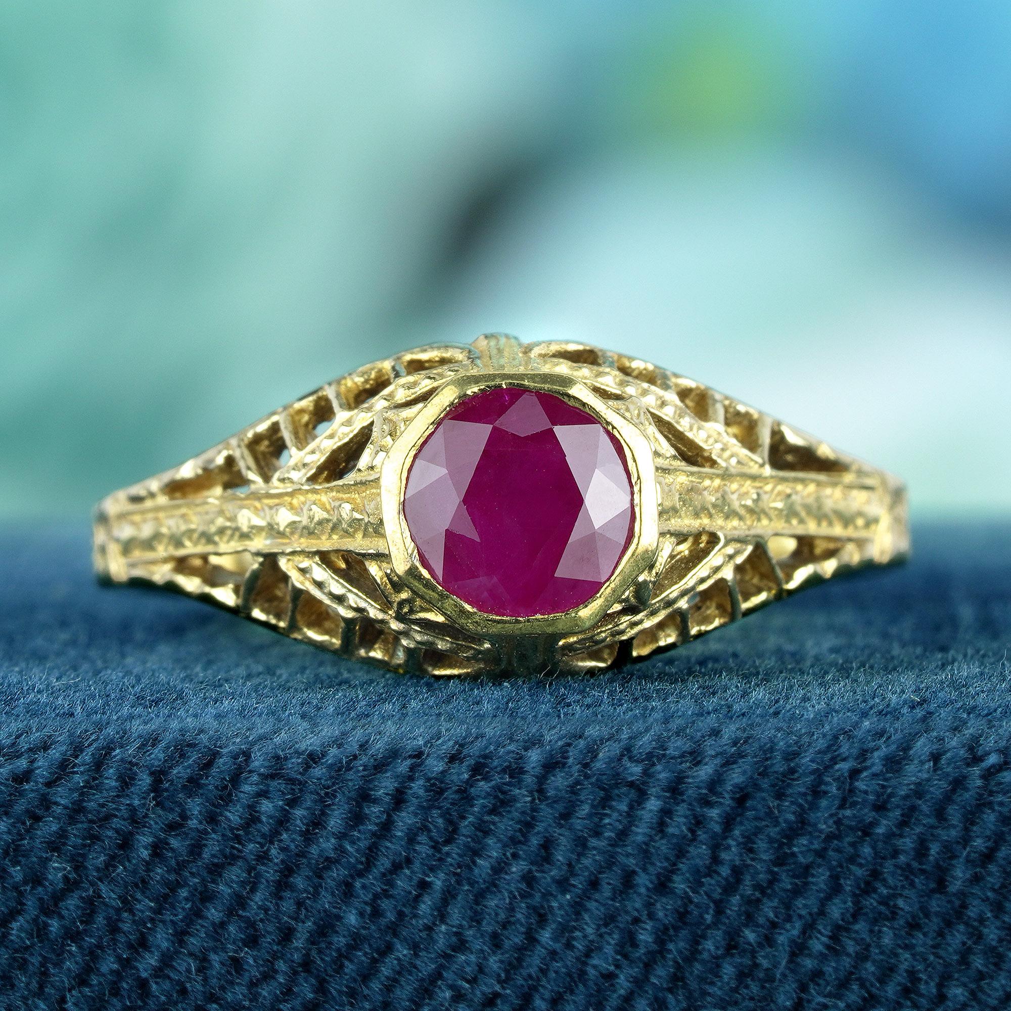 This vintage-inspired filigree ring centerpiece is a round ruby, shown  its deep red hue and smooth, domed surface. This ruby is set amidst a backdrop of yellow gold, which is adorned with intricate vintage-style patterns, enhancing the ring’s