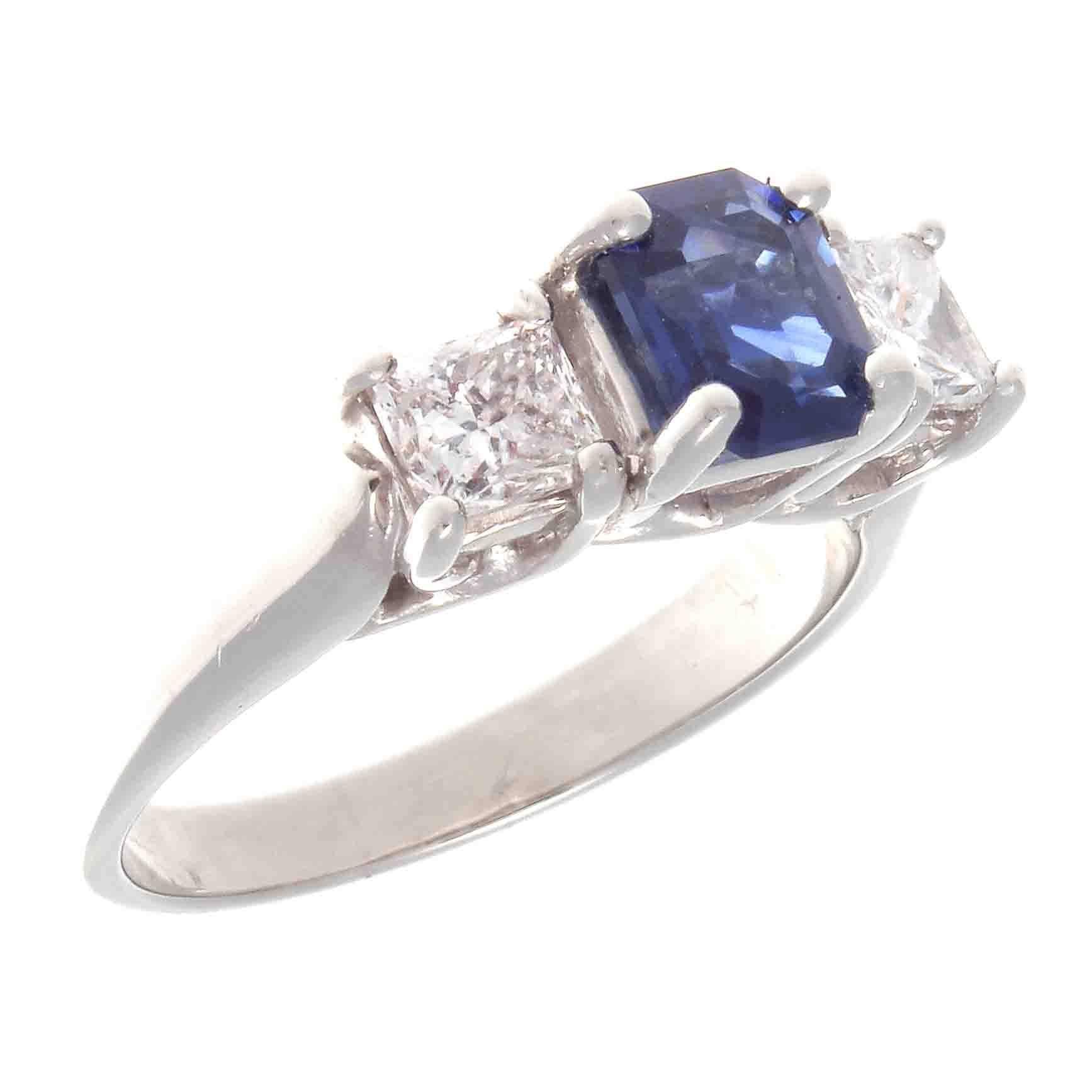 A classic creation of style and grace that has survived many decades of change. Featuring a vivid royal blue emerald cut sapphire that weighs approximately 1.10 carats. Perfectly complimented on either side by a single near colorless princess cut