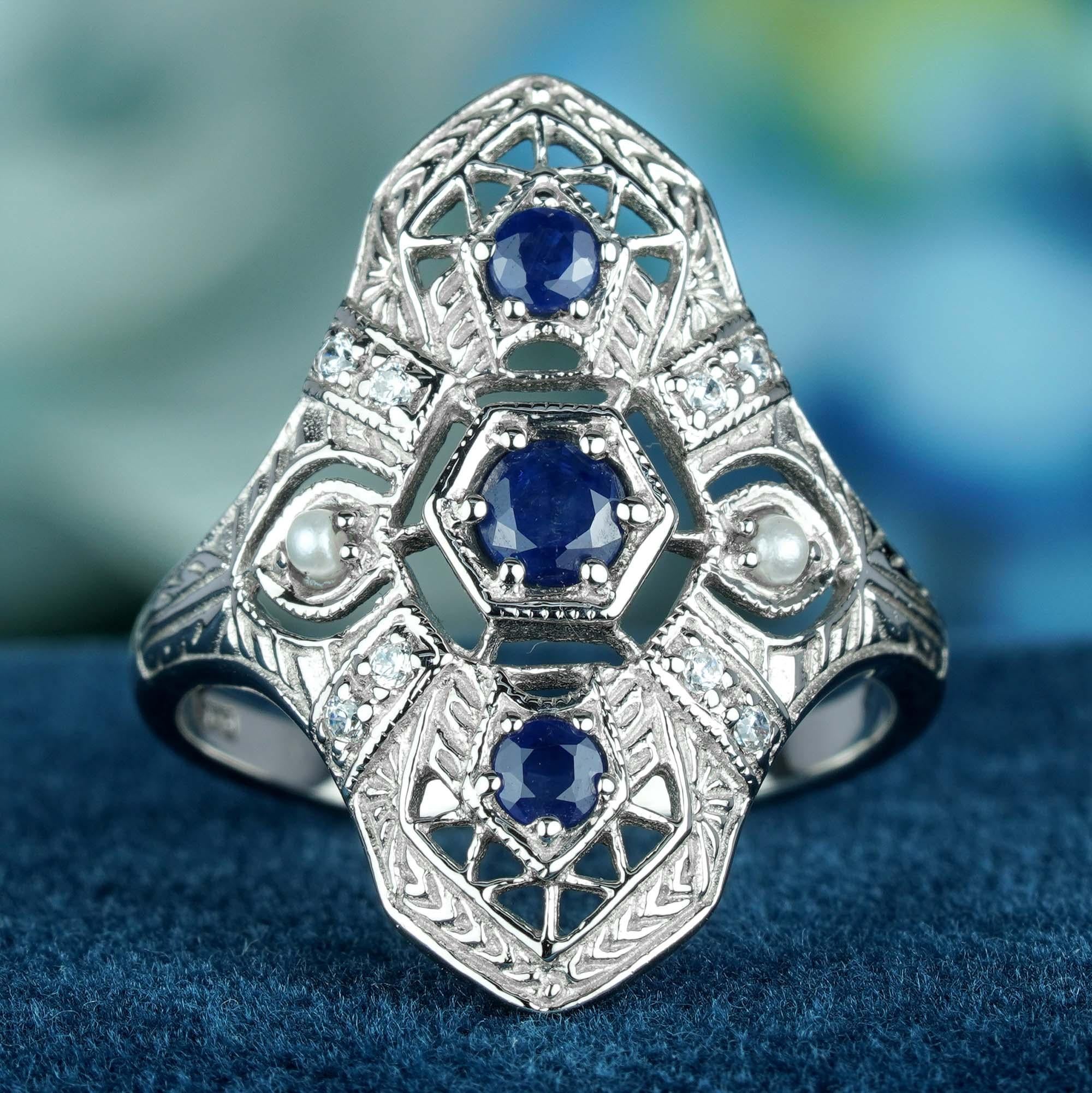 Dieser Ring im Vintage-Stil des Art déco. In der Mitte befinden sich 3 kaskadenförmig angeordnete runde blaue Saphire, die in einer erhöhten Lünette gefasst sind. Zarte Filigranarbeiten schmücken das massive Weißgoldband und die Schultern und