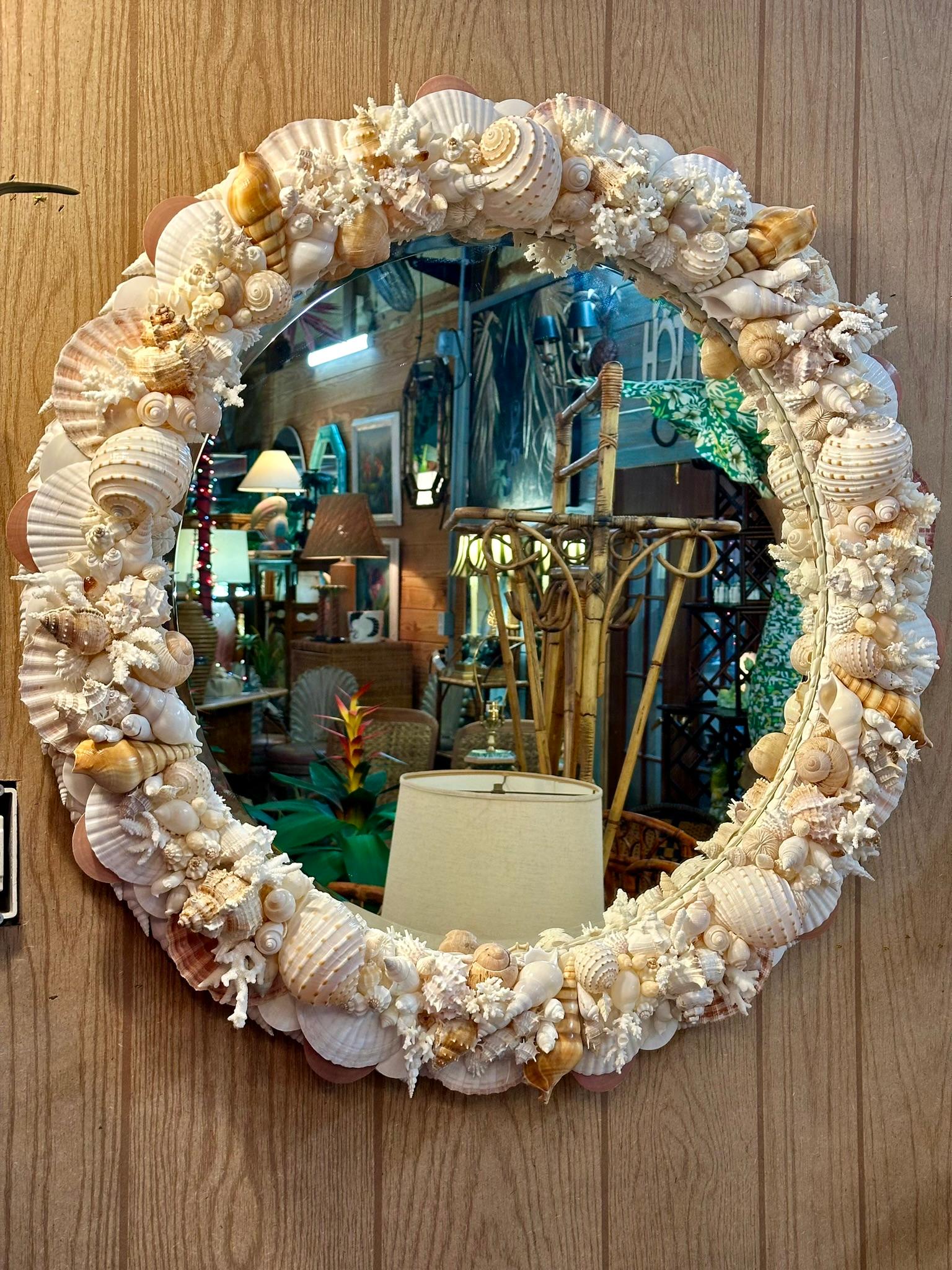 Introducing an exquisite handmade seashell-encrusted round wall mirror, ready to hang with a heavy gauge wire. This incredible sculptural piece features layers of intricately placed seashells, including Tonna, Tibia, nutmeg, and coral, accented with
