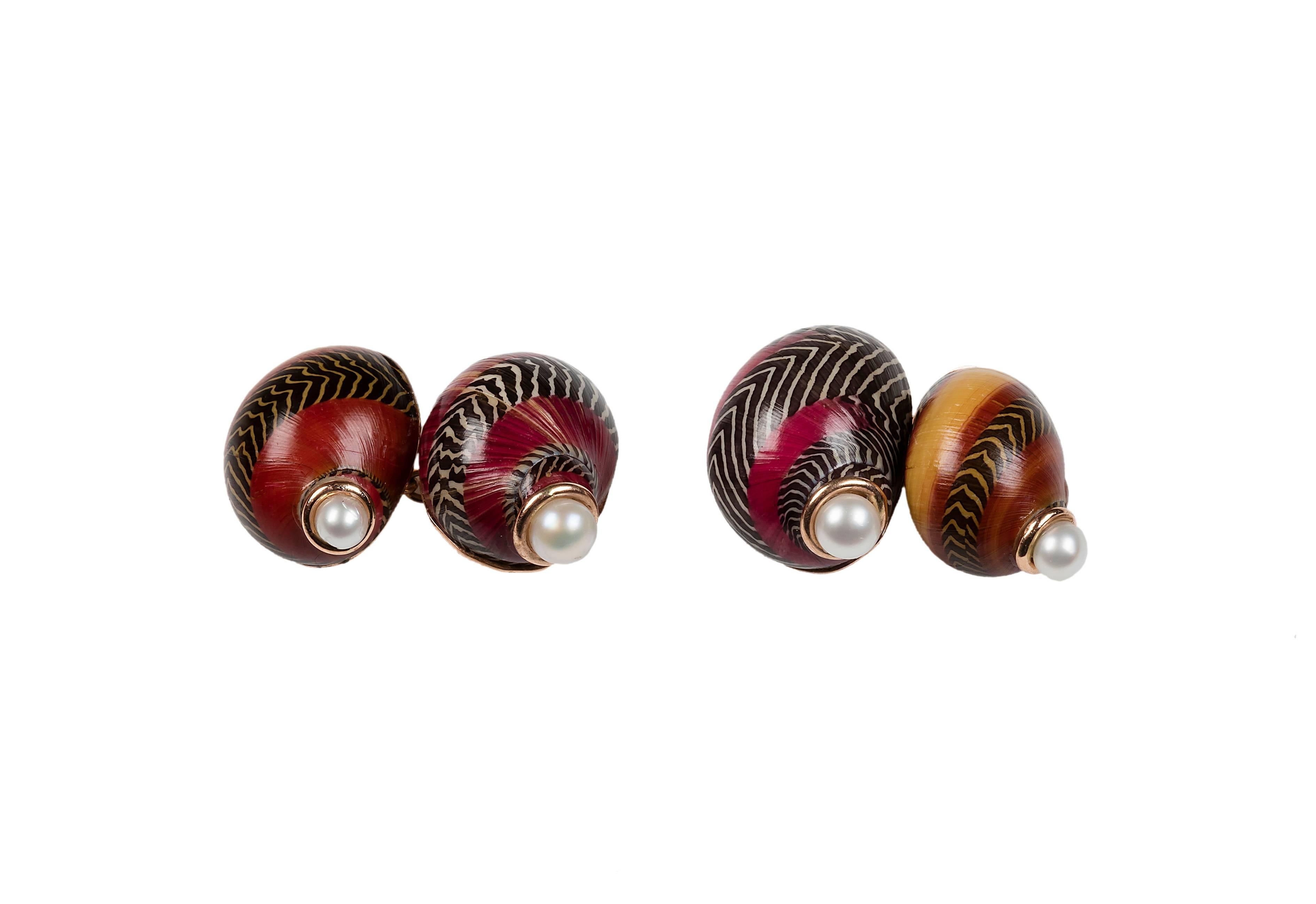 These striking cufflinks feature a matching front face and toggle made both of a Red Nerita shell. 
The natural patterns and bright colors of the shells are adorned with a simple pearl each, while the post that links the two parts is in 14 karat