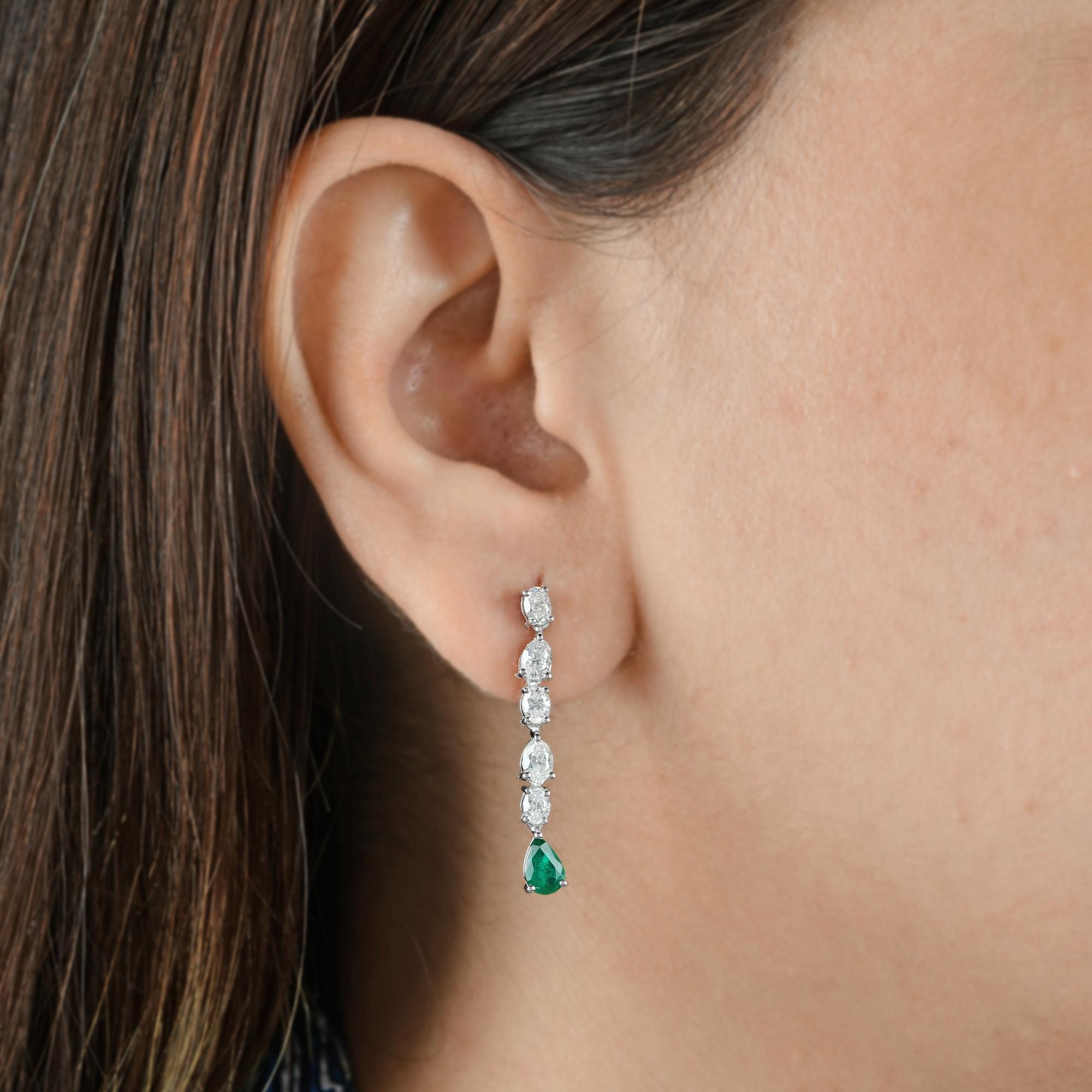 Ces boucles d'oreilles pendantes en or blanc 14 carats avec diamants SI/H naturels et émeraudes de Zambie présentent deux émeraudes taillées en poire qui pendent à l'extrémité des longues boucles d'oreilles en diamants.
Les émeraudes sont des
