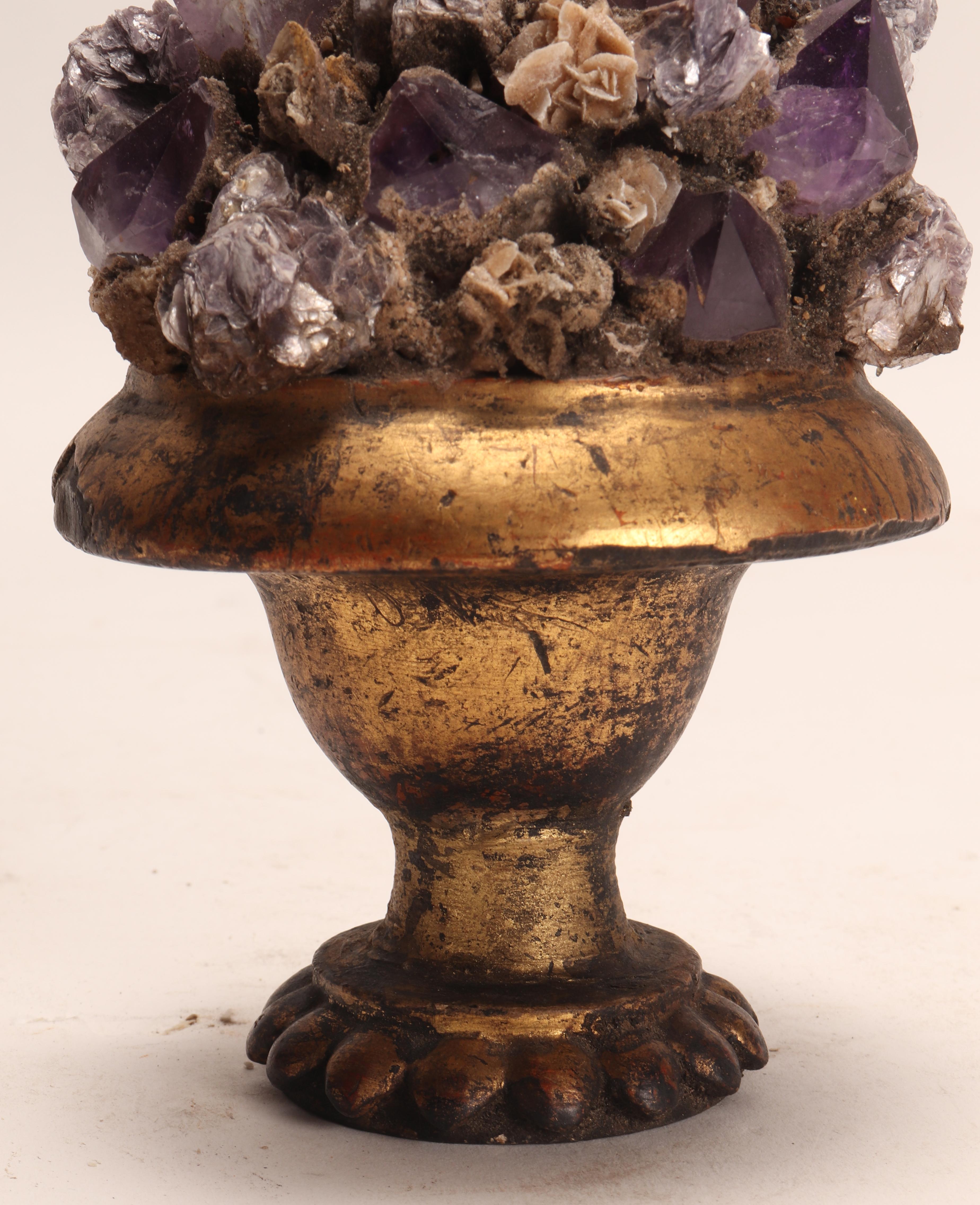 A Naturalia mineral specimen. A druse with amethyst, mica and desert rose crystals, mounted over a guild-plated wooden base on a vase shape. Italy circa 1880.