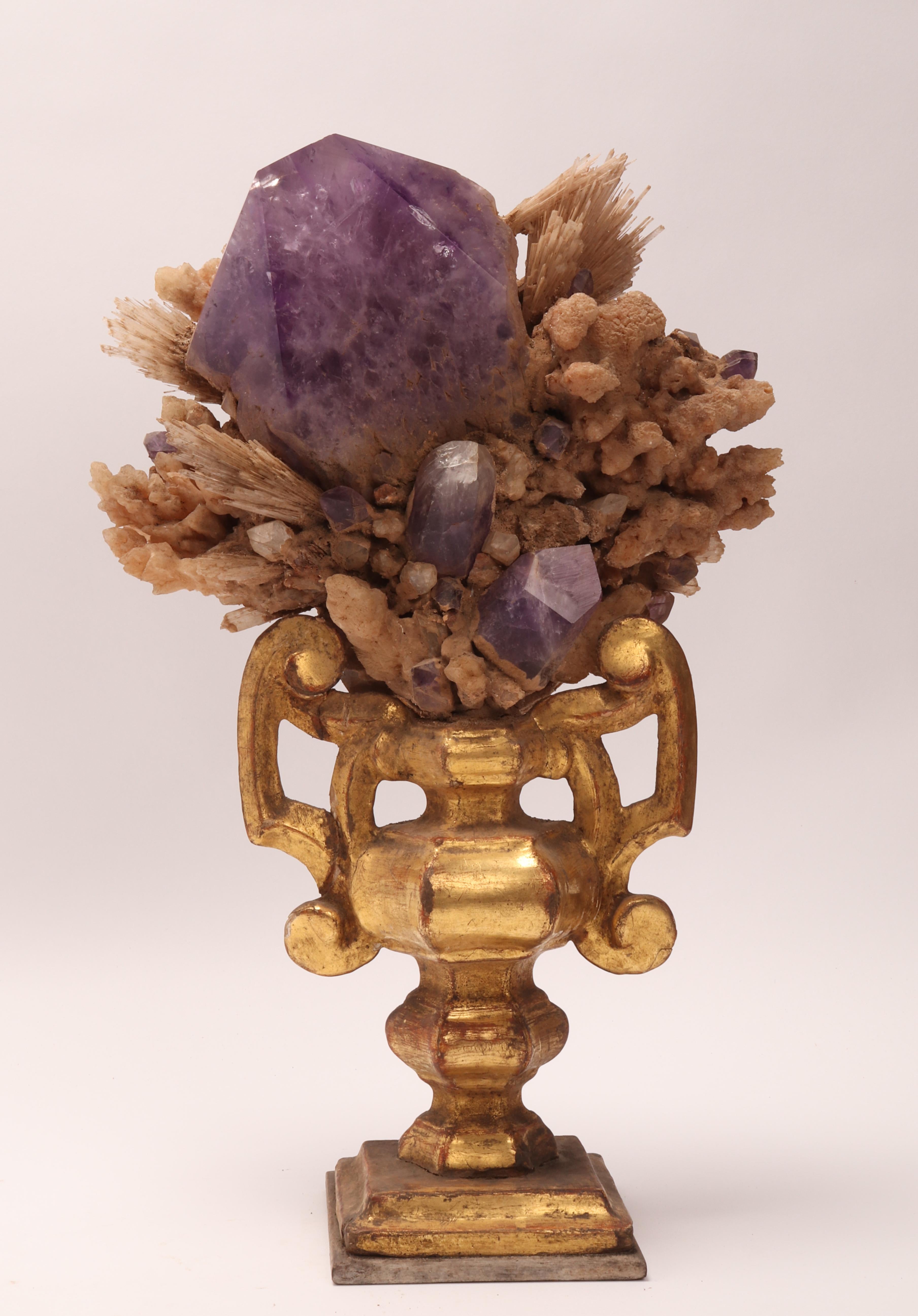 A Naturalia mineral specimen. A druze of Amethyst, colacite stones and calcite flowers crystals, mounted over a guild-plated wooden base on a vase shape. Italy 1880 ca.