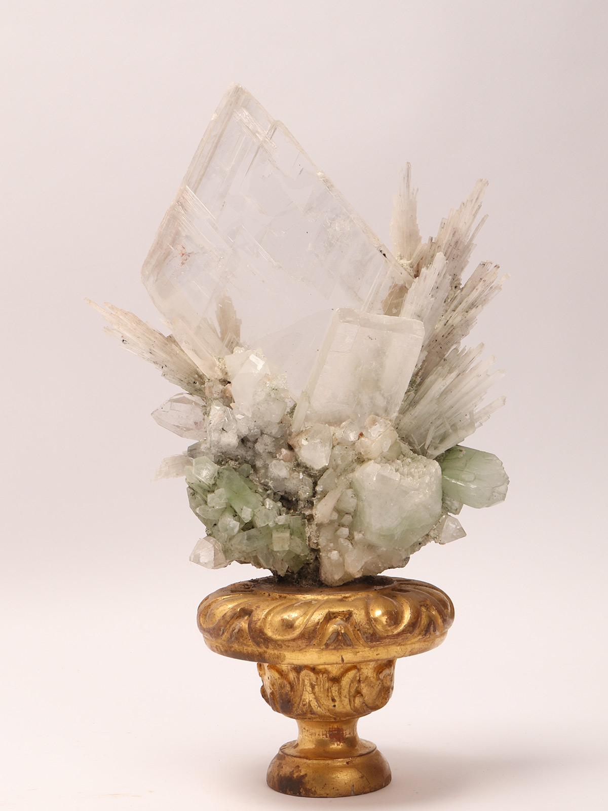 A Naturalia mineral specimen. A druse of apophilite, quartz, colacite and calcite flowers crystals, mounted over a guild-plated wooden base on a vase shape. Italy 1880 ca.