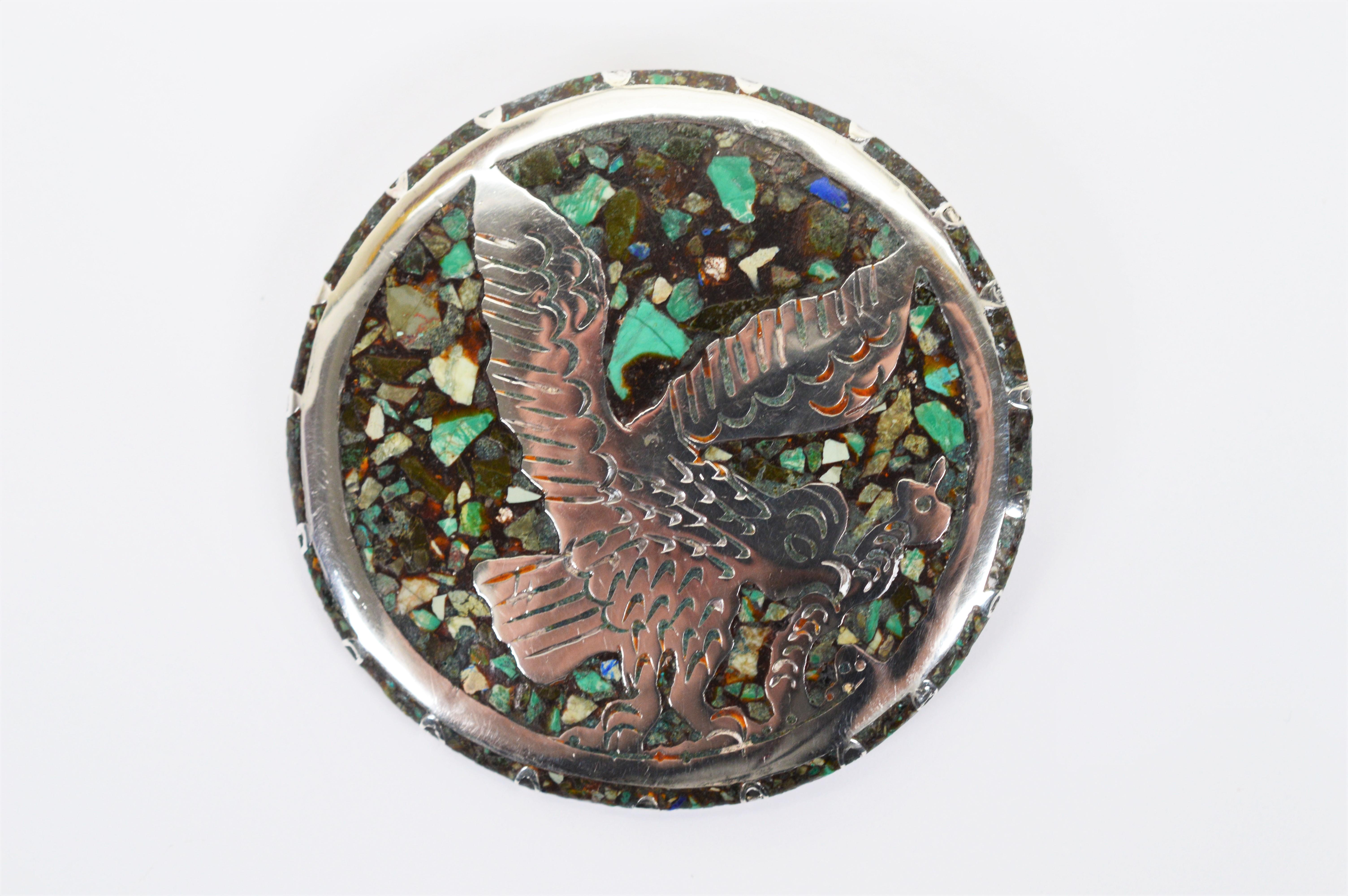A colorful mosaic of natural stone inlay encircles a bird of prey on this earthy sterling silver brooch. Round, measuring 2-1/4 inch in diameter, this interesting hand hammered artisan piece from Mexico is fitted with a pin to wear as a brooch and a