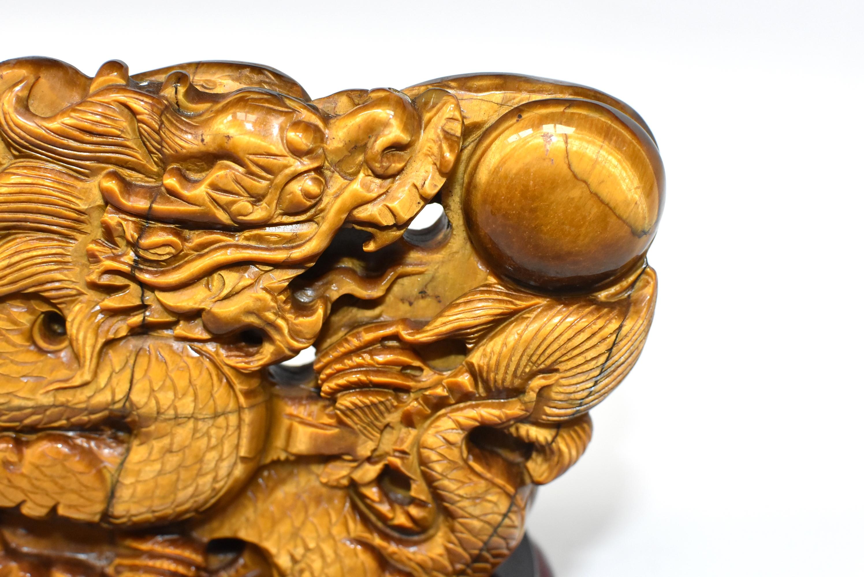 A stunning natural tiger's eye sculpture depicting a dragon chasing a ball. Amazing iridescence. Sculpture is one piece of natural tiger's eye of the finest grade. Fine carvings make the dragon come to life. Solid wood custom stand. One of a kind.