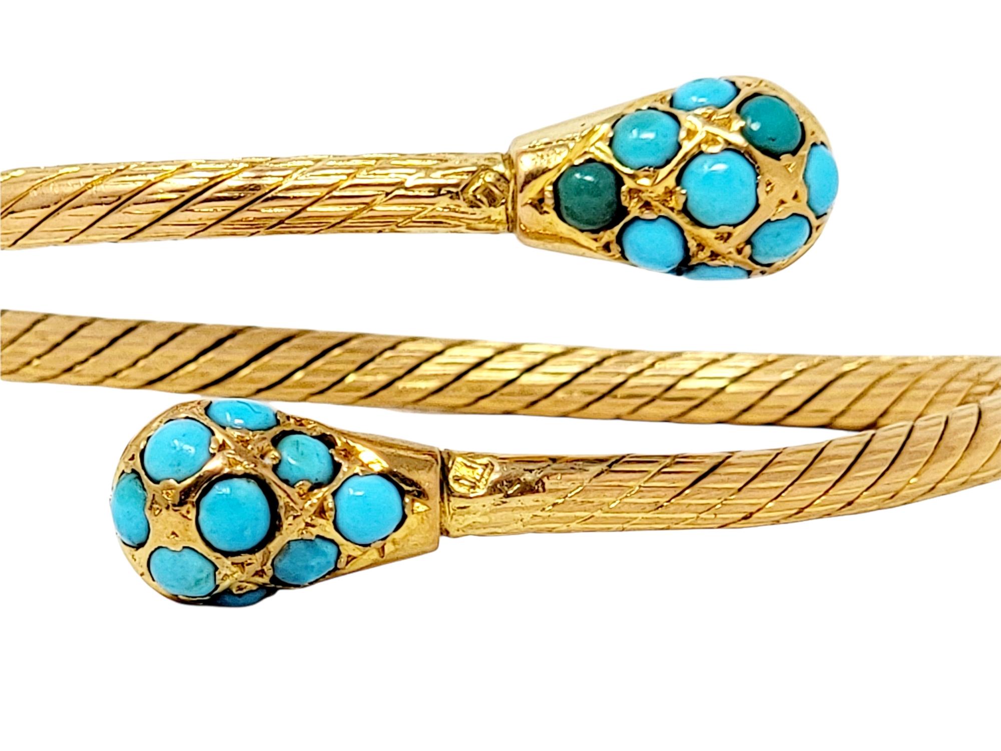 Gorgeous bypass style bracelet features 18 cabochon turquoise stones set in rounded 18 karat yellow gold ends. The stunning natural stones all vary slightly in color, showcasing their stunning blueish-green hues. The narrow band of the flexible