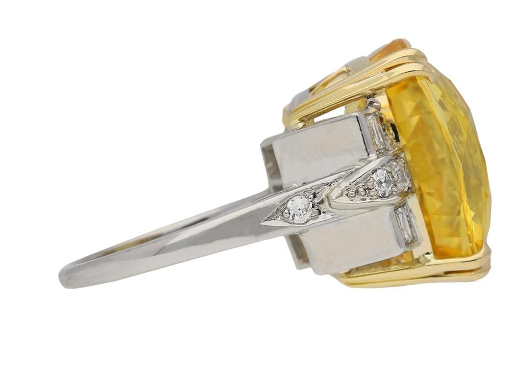 Yellow Ceylon sapphire and diamond ring. Set with a cushion shape old cut natural unenhanced yellow Ceylon sapphire in an open back four split claw setting with an approximate weight of 21.00 carats, flanked by four square step cut diamonds in open