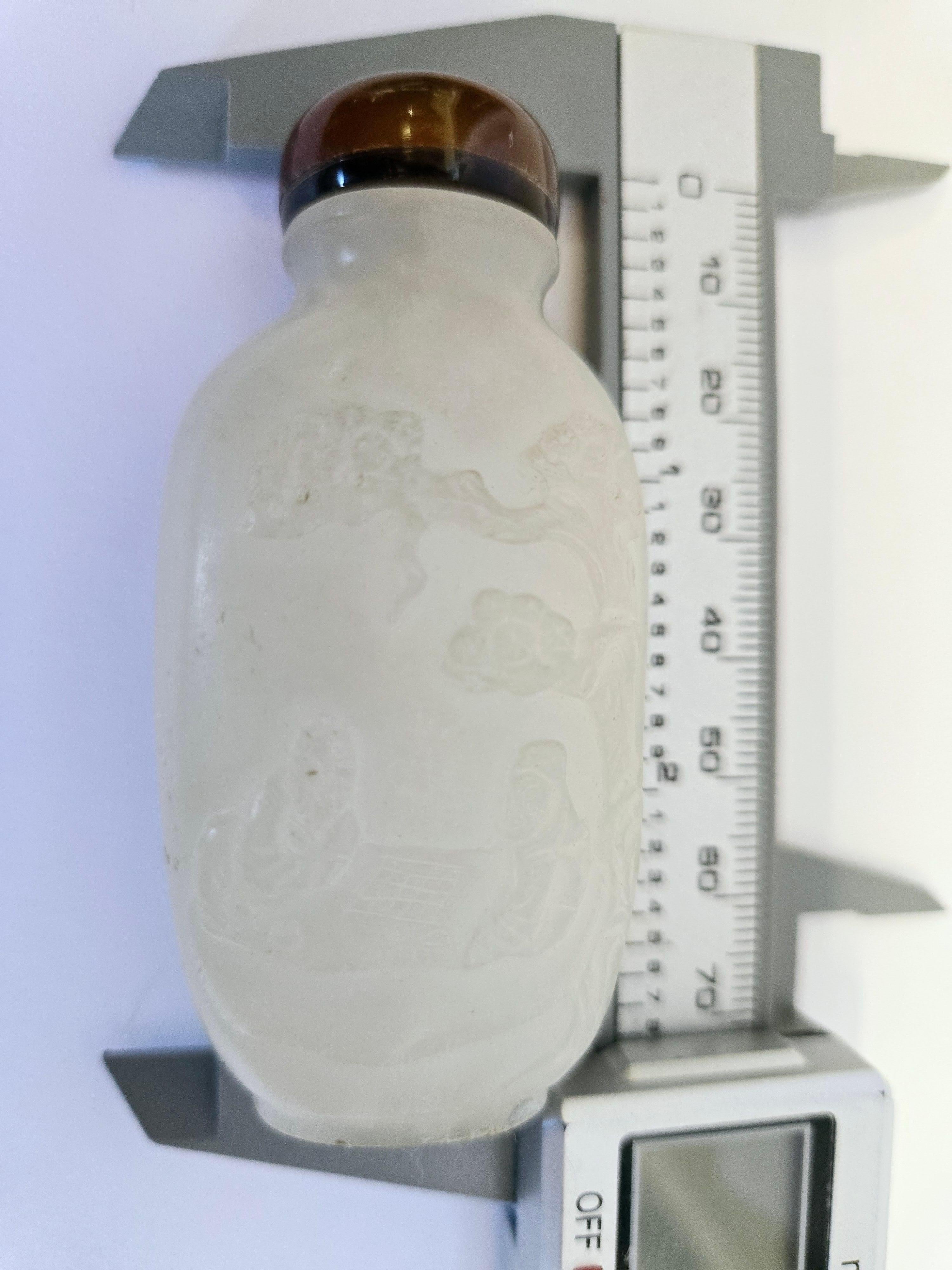 Sculptée de manière experte dans du jade blanc naturel, cette tabatière présente des scènes complexes sur ses deux faces. L'une des faces présente une fillette enjouée, symbolisant la joie et l'innocence, tandis que le verso présente deux figures de