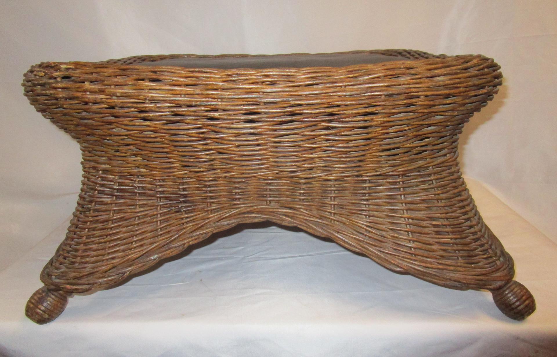 This handsome natural wicker footstool is woven with round reed in a rolled edge fashion with closely woven skirting. Features include flared ball feet of turned wood to simulate wicker wrapping. The seat is leather and looks to be original.
