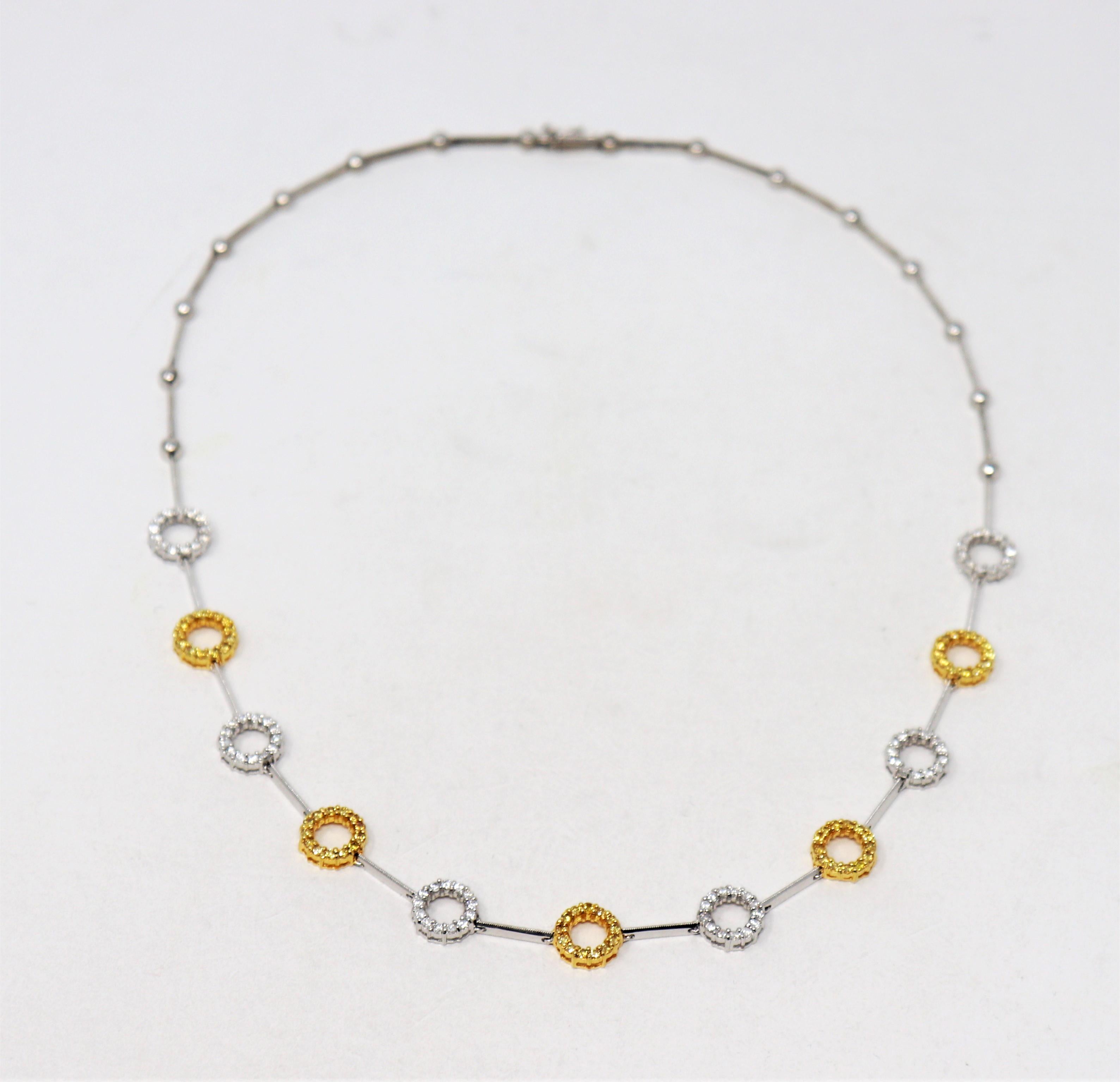 Dies ist eine schöne zweifarbige Halskette mit glitzernden, gepflasterten Diamanten. In den zarten, offenen Kreisen wechseln sich naturweiße und gelbe Steine ab, die durch schlanke, polierte Glieder miteinander verbunden sind. Ein wirklich