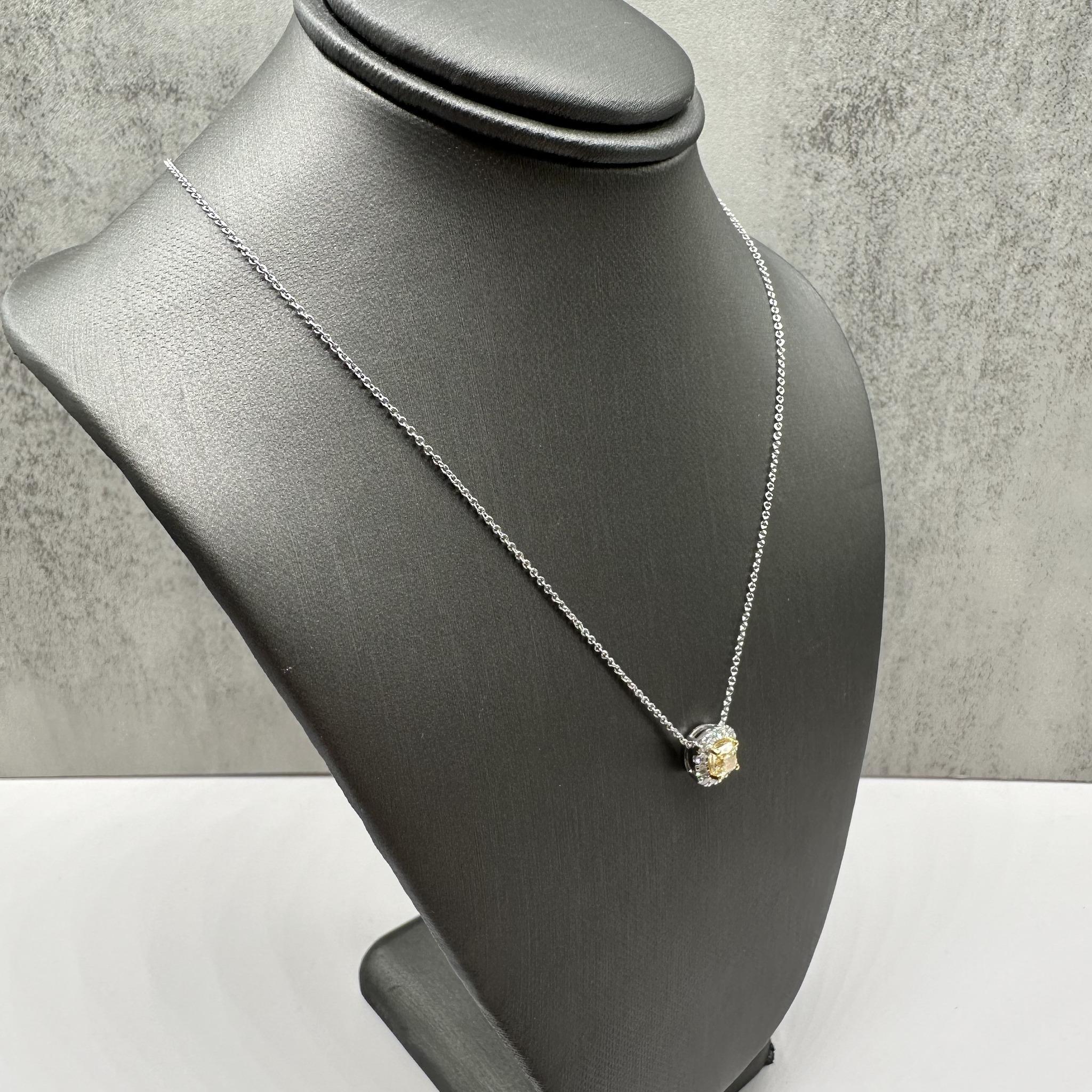 This stunning Natural Yellow Diamond Pendant Necklace in 14kt gold features a 0.67ctw natural fancy light yellow cushion-cut diamond at the center, surrounded by 0.23ctw of natural GH VS/SI round diamonds. The pendant is set in white gold, with the