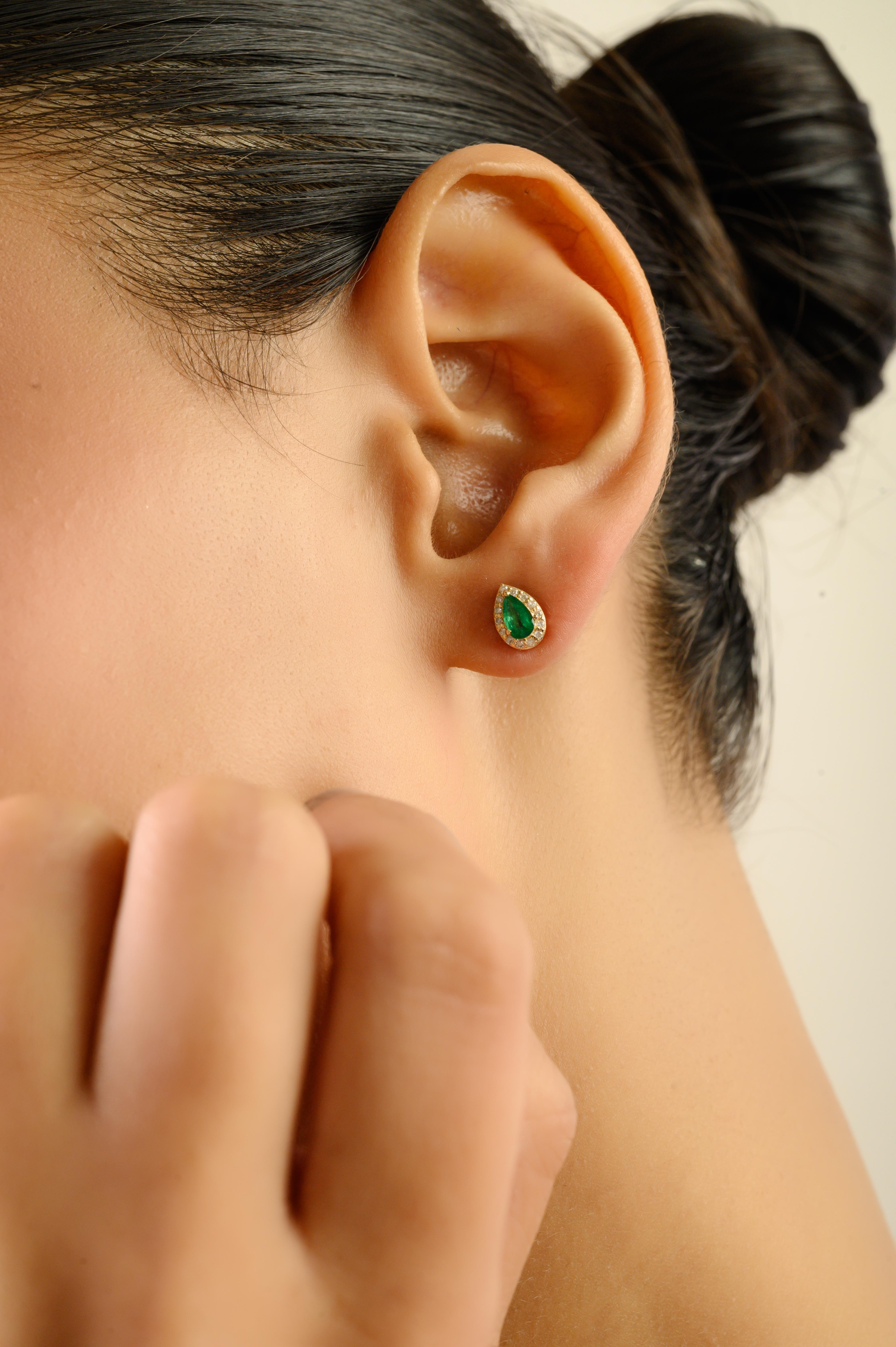 Ces élégantes boucles d'oreilles en or jaune 14 carats mettent en valeur deux émeraudes zambiennes naturelles taillées en poire totalisant 0,34 carat, chacune mesurant environ 5×3 mm. Chaque émeraude est entourée d'un halo radieux de diamants ronds