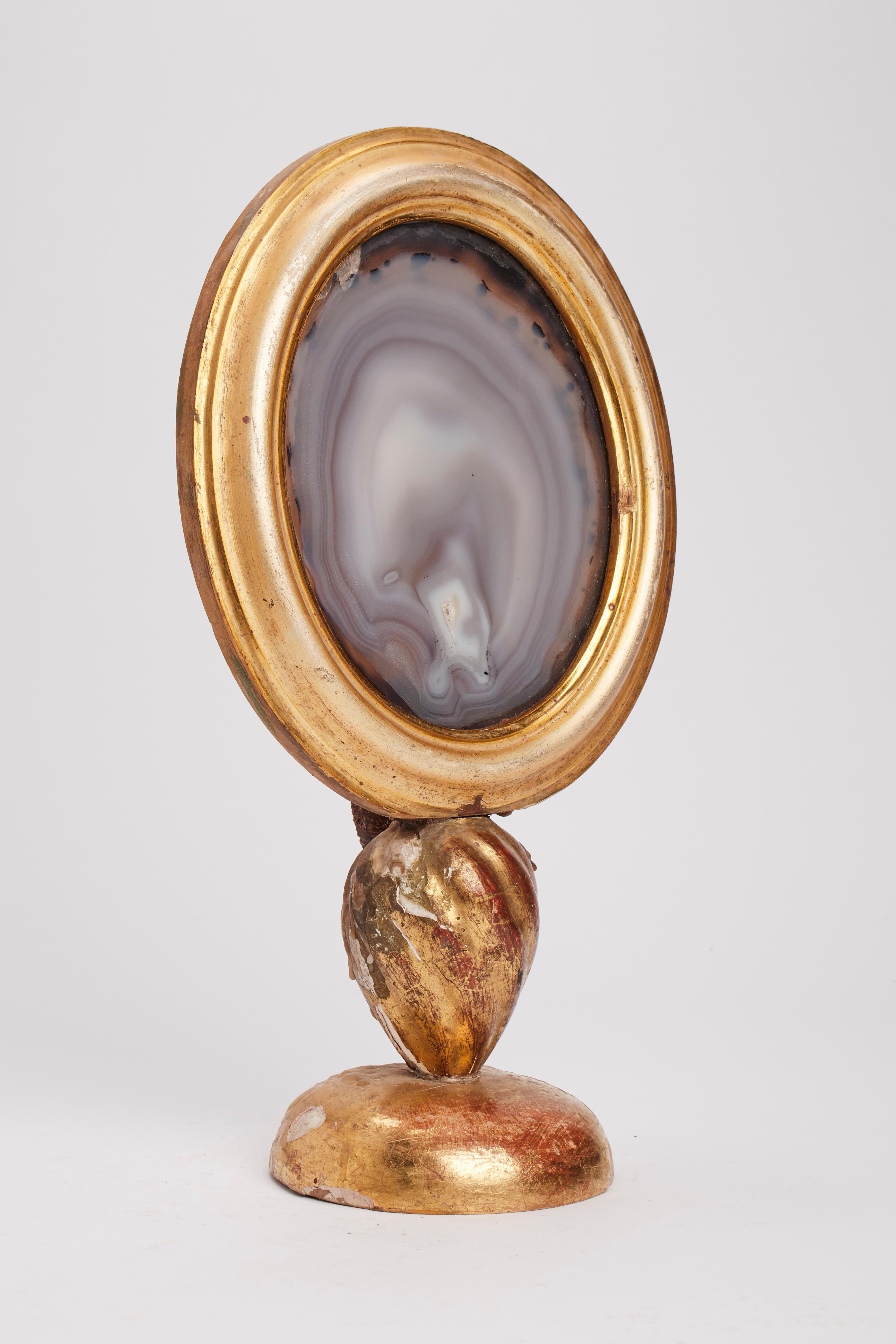 A Wunderkammer naturalia agate specimen mounted in an oval shape frame over a golden wooden base, with a candleholder, Italy, circa 1880.