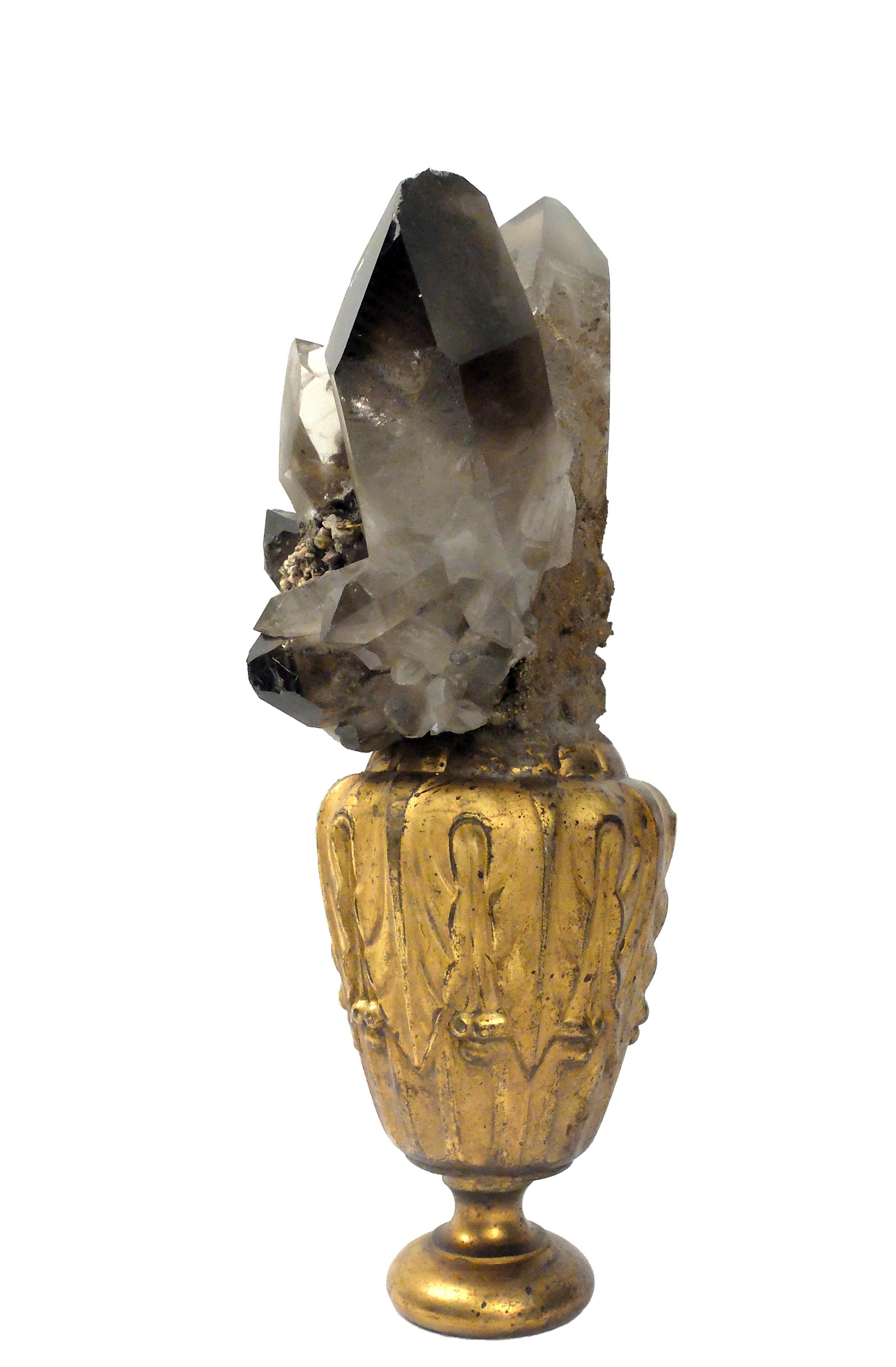 A naturalia mineral specimen: A composition with smoky quartz and axinite crystals, mounted over a guild plated wooden base on a vase shape with leaves decoration.