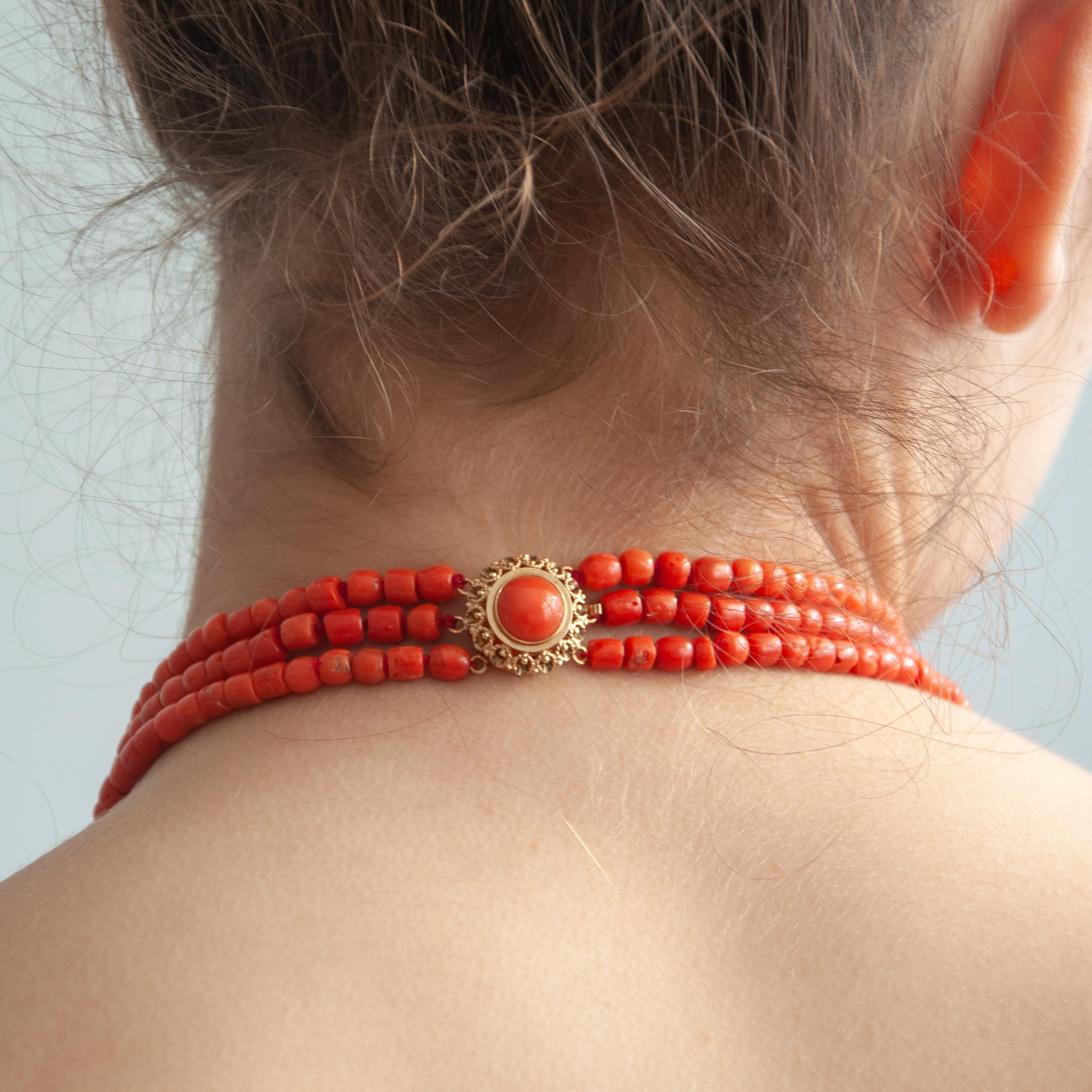 A 14 karat yellow gold three-strand natural red coral beaded necklace. The necklace has a beautiful round gold filigree clasp set with a round cabochon cut coral stone. The corals on this multi-strand necklace are barrel-shaped and have a diameter
