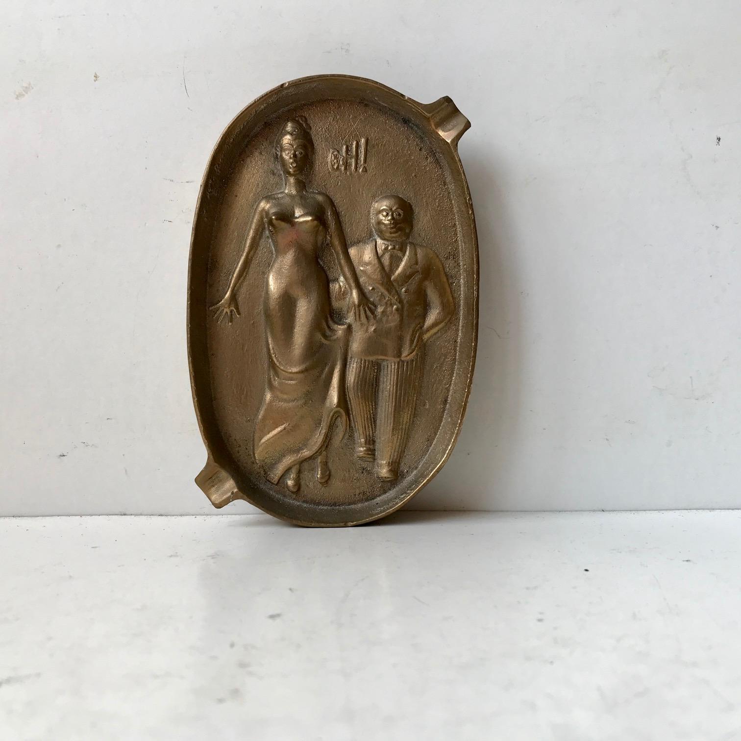 Oval double sided bronze 'ash'- tray featuring a woman exclaiming “Oh!” with two cigarette rests. On the reverse we see that the man has his hand up the woman’s skirt. Manufactured in the style of similar pieces made during the Victorian era.