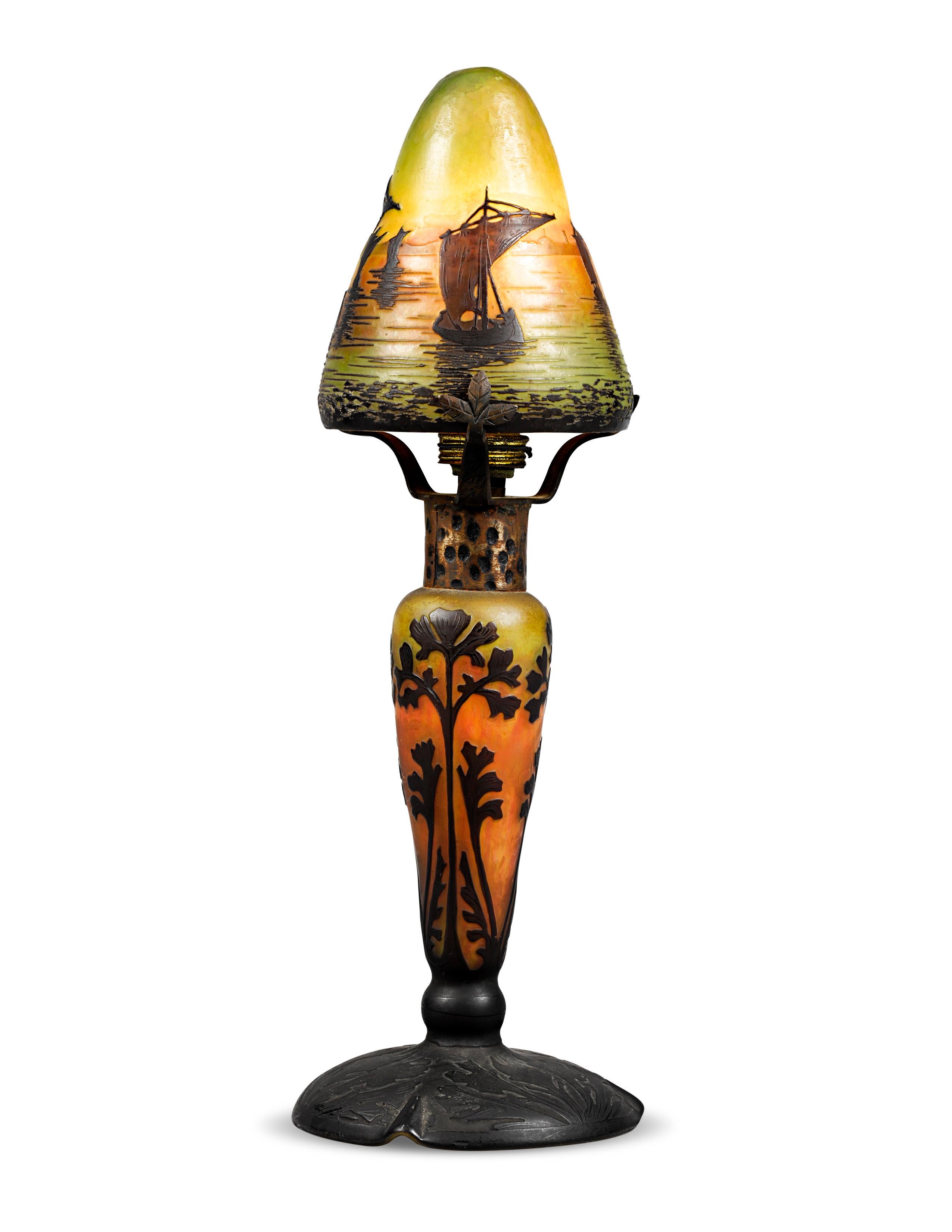 This cameo glass lamp by the renowned French glassmaking firm Daum Nancy casts an alluringly warm glow. Careful wheel-carving and acid-etching reveal layers of vibrant color, and the stunning nautical motif lends drama to the colorful background.