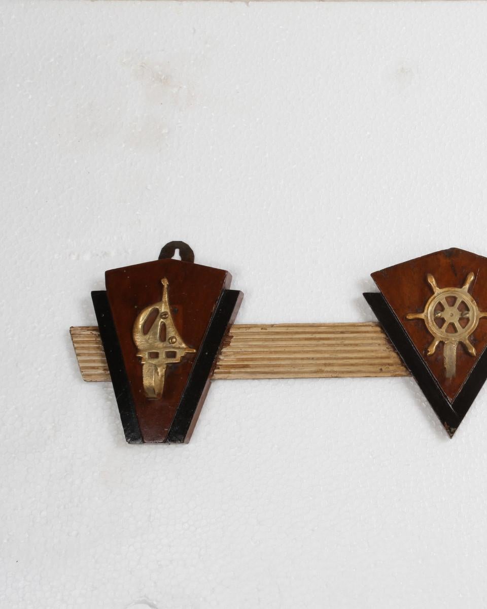 A group of teak, rosewood and brass coat hooks with nautical motifs. Reeded and painted bar with brass nautical hooks mounted on beveled rosewood and teak back-plates. Salvaged from a decommissioned, 1970s cruise ship.