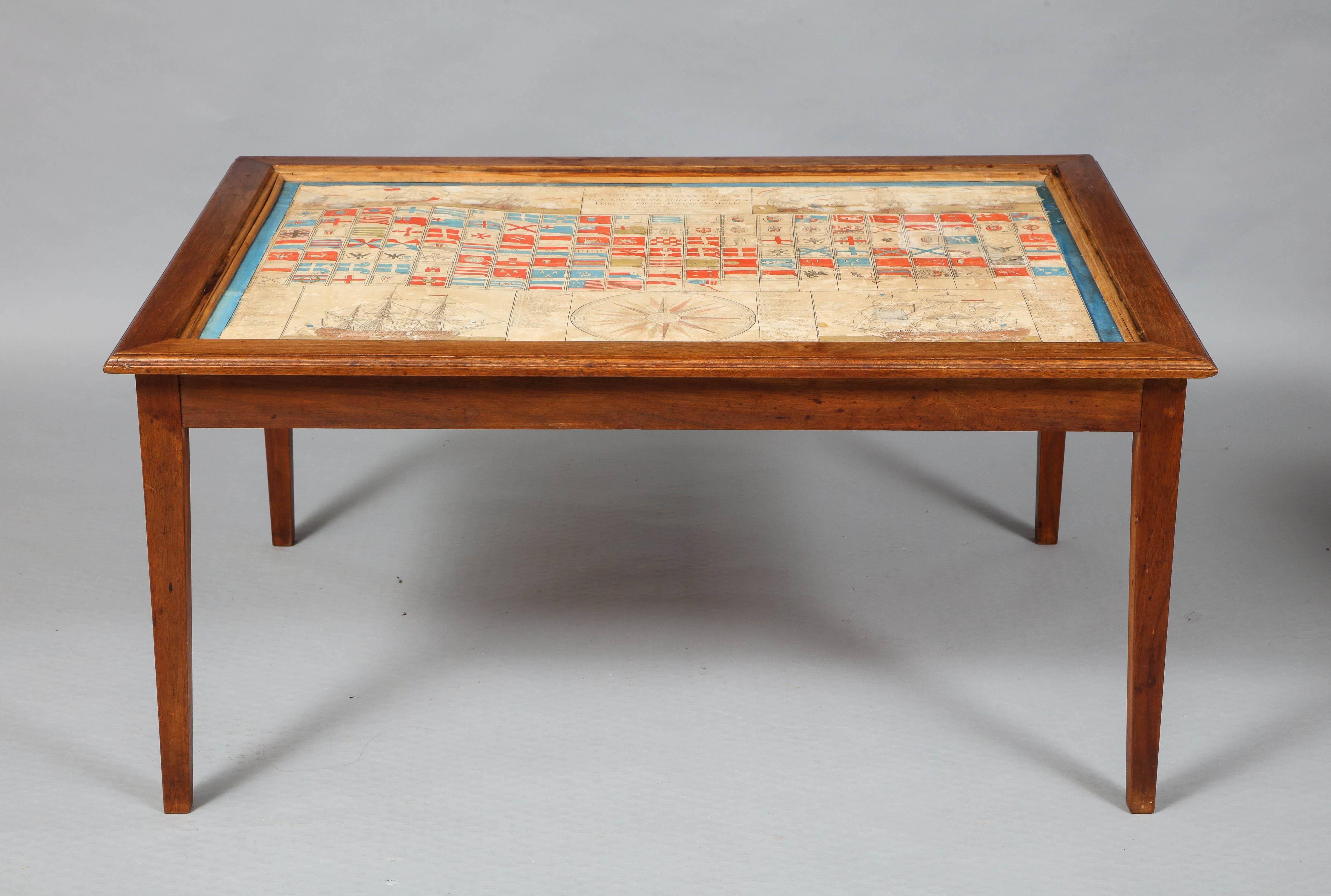 Unusual midcentury walnut coffee table incorporating a hand colored 18th century French engraved chart of naval flags, dated 1782. The top of mitered walnut with engraving under glass top, standing on square tapered legs in a pale walnut. The