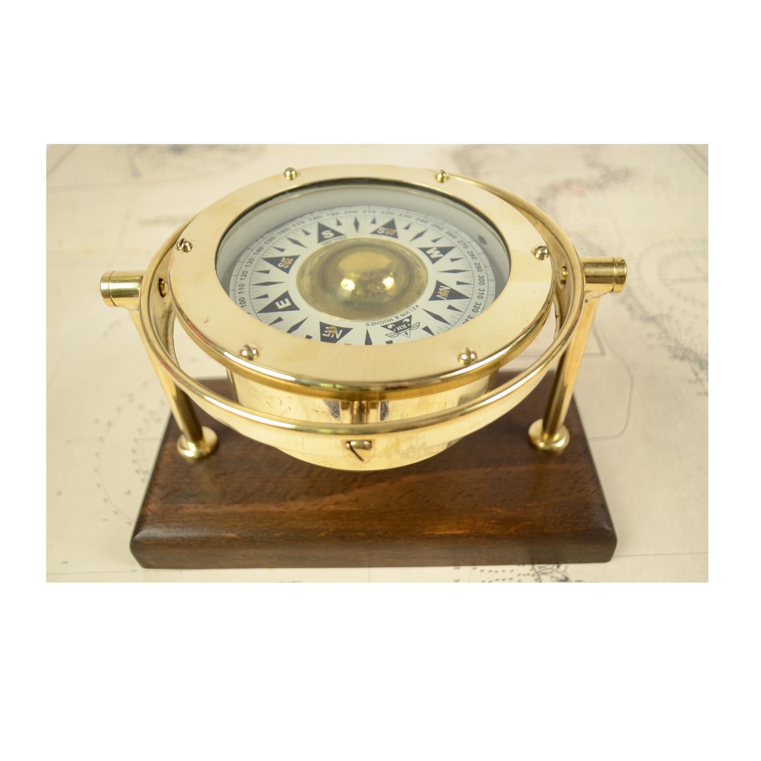 Nautical liquid compass, brass, on universal joint, mounted on wooden board. Made by Kelvin & Hughes Limited at the end of the 1940s. The compass has a cylindrical brass container, on the bottom of which a stem of hard metal is fixed, on which there