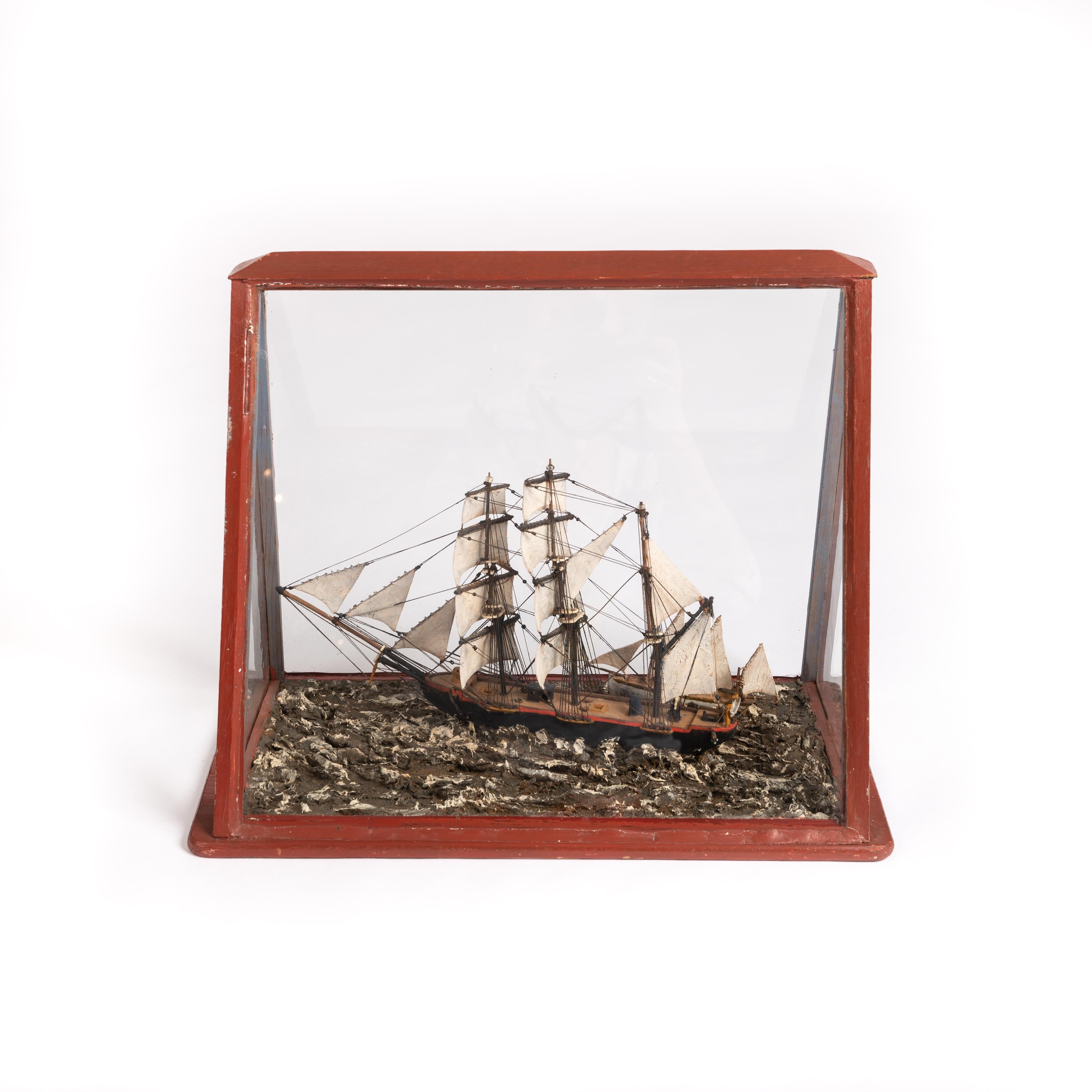 Nautical display in showcase France beginning 20th century.
The object is finely handcrafted from wood, plaster, fabric and paint. It shows an antique sailing ship on the high seas. 
Unusual about the object is the red trapezoidal