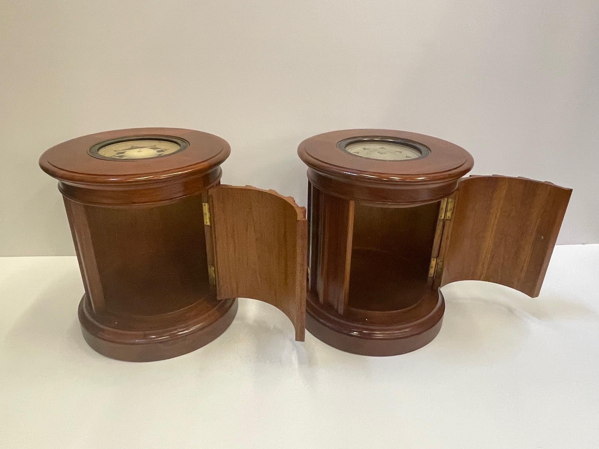 A sublime custom made rare pair of carved mahogany round end tables having authentic antique compasses inset under glass on top. Each nautical style table has a single door that opens for storage within.