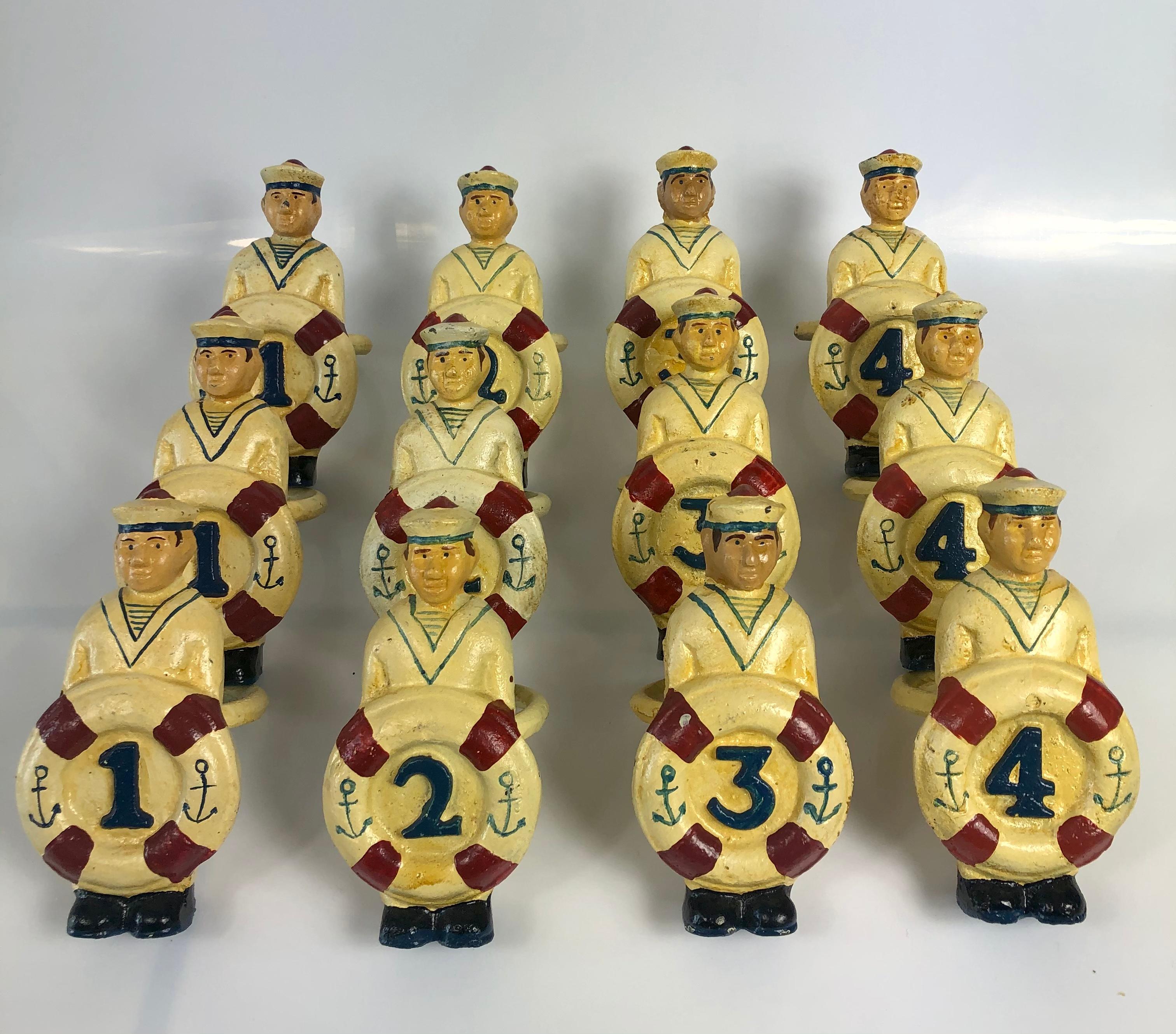 Rare vintage hand painted iron sailor napkin rings featuring a sailor. He is dressed in off white (that has yellowed) standing at attention while holding an life ring preserver that is with 4 red lines and two anchors. In the middle of the life ring