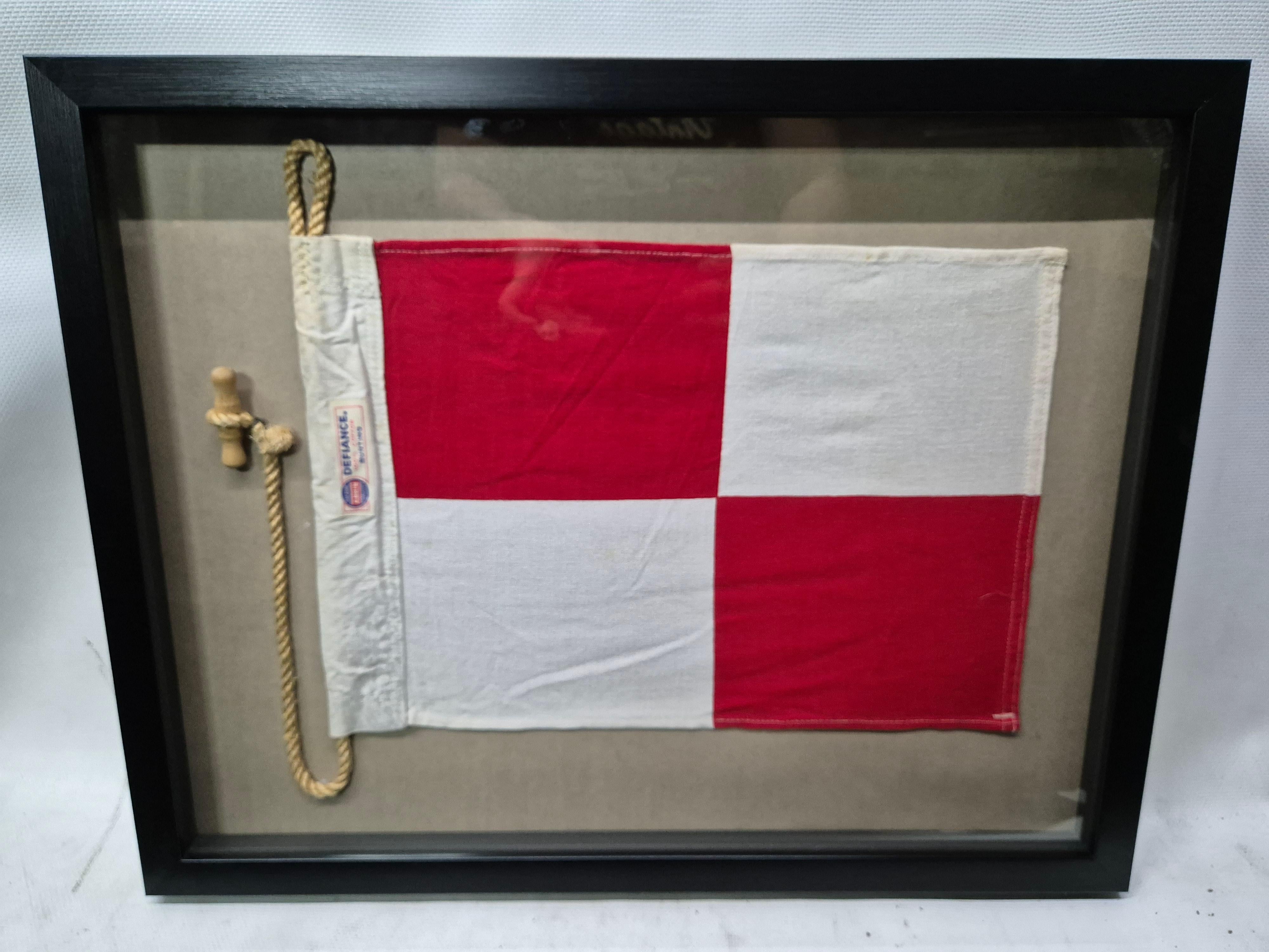 International maritime signal flag of letter 'U' set into a shadowbox frame. The cotton flag has a white canvas hoist with a sisal rope and wood toggle, with a maker's label from flag maker 