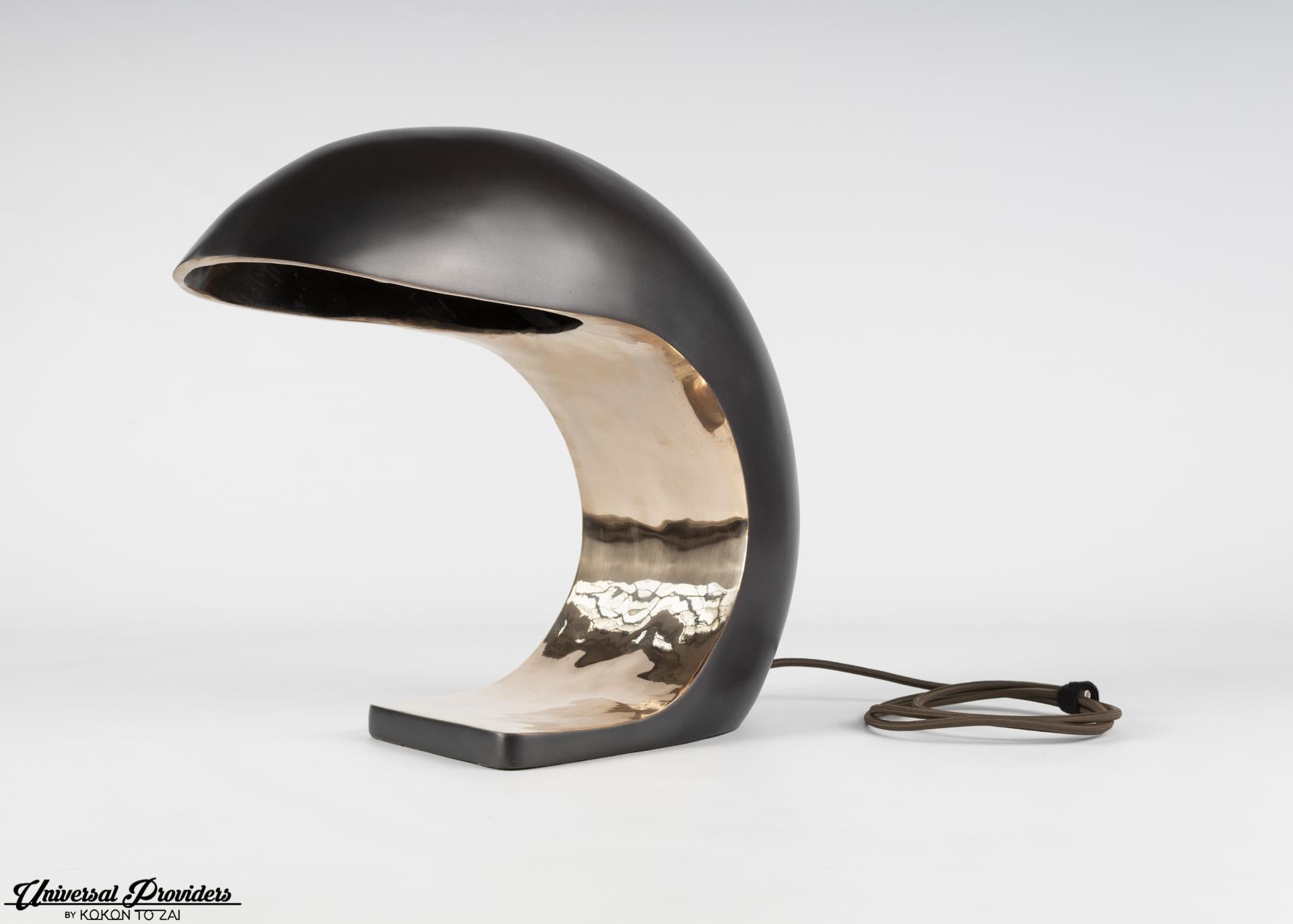 The Nautilus Study table lamp is inspired by midcentury Italian design. It is cast bronze and weighs up to 28 pounds. The outer shell has a blackened patina, and the face is high polished to a mirrored finish. The Nautilus illuminates by a three-way