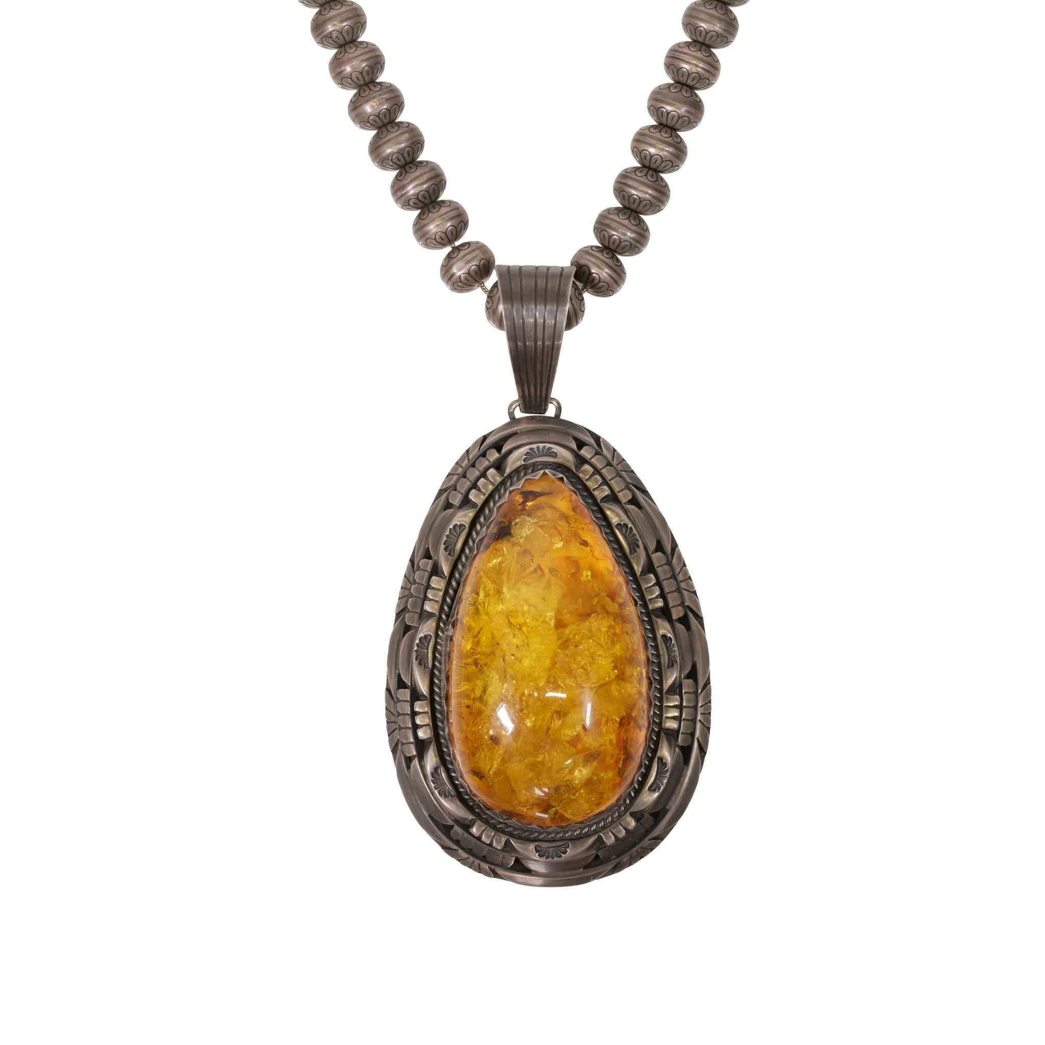 Solid amber pendant necklace. Marked Sterling, signed Charles Johnson. Stunning giant amber, beautiful antique chain, lightweight for the size. Chain is detailed with hand stamped decorated beads.

PERIOD: After 1950

ORIGIN: Navajo,