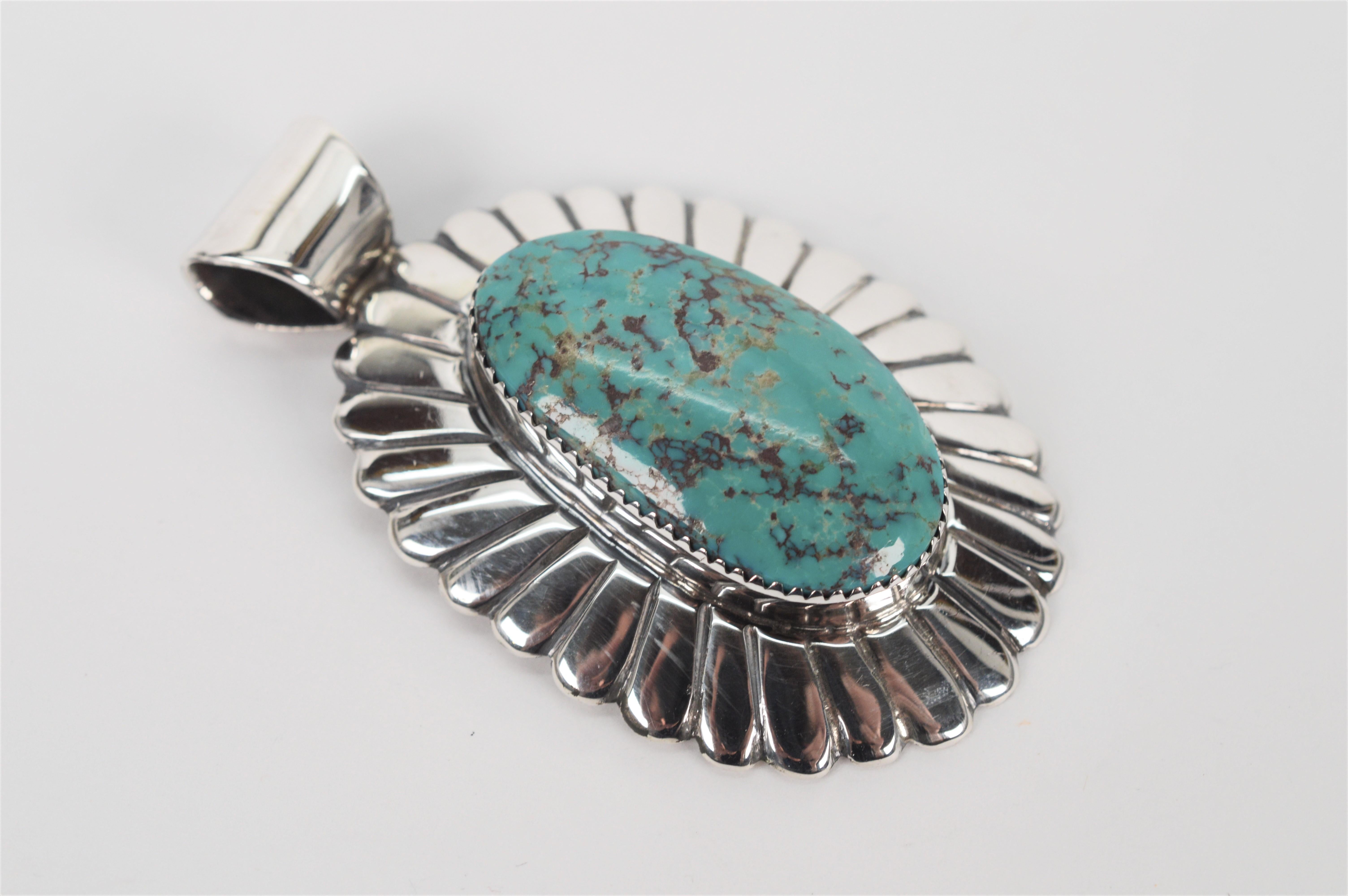 An impressive 18 x 33mm natural turquoise cabochon is featured on this thick gauge scalloped sterling silver pendant crafted by known Navajo silversmith, Arnold Blackgoat. Measuring two inches in length plus the bail and 1.5 inches in width, this