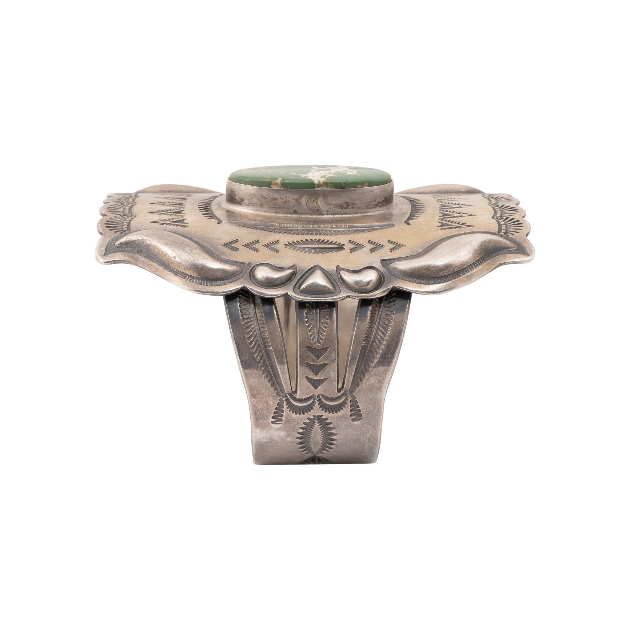 Navajo Carlin Mine turquoise and sterling silver cuff bracelet. Center stone set in solid sandcast shield with hand stamp palmettes. Stone is a deep green color with gold and beige matrix. Intricate geometric details on front and sides. Maker's