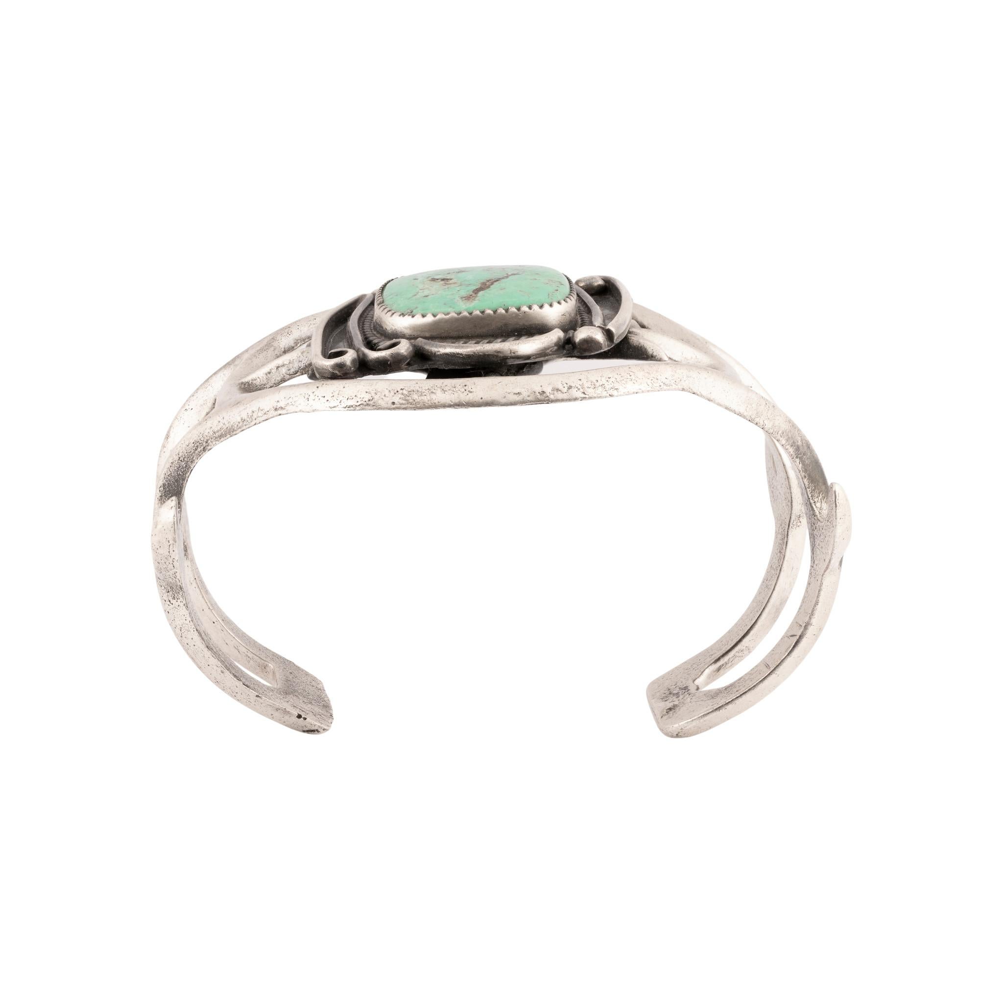 Bracciale in turchese Cerrillos e argento fuso con sabbia. Pietra singola incastonata in un castone a dente di sega con bordo in corda ritorta, in una scatola asimmetrica con disegni a volute. La pietra è di colore verde brillante con matrice